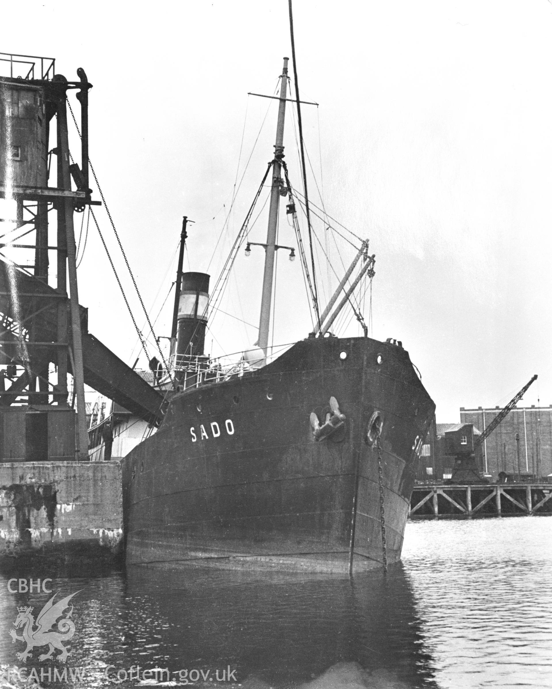 Black and white photograph showing the vessel SADO alongside one of the bulk loading quays on the western side of the harbour.