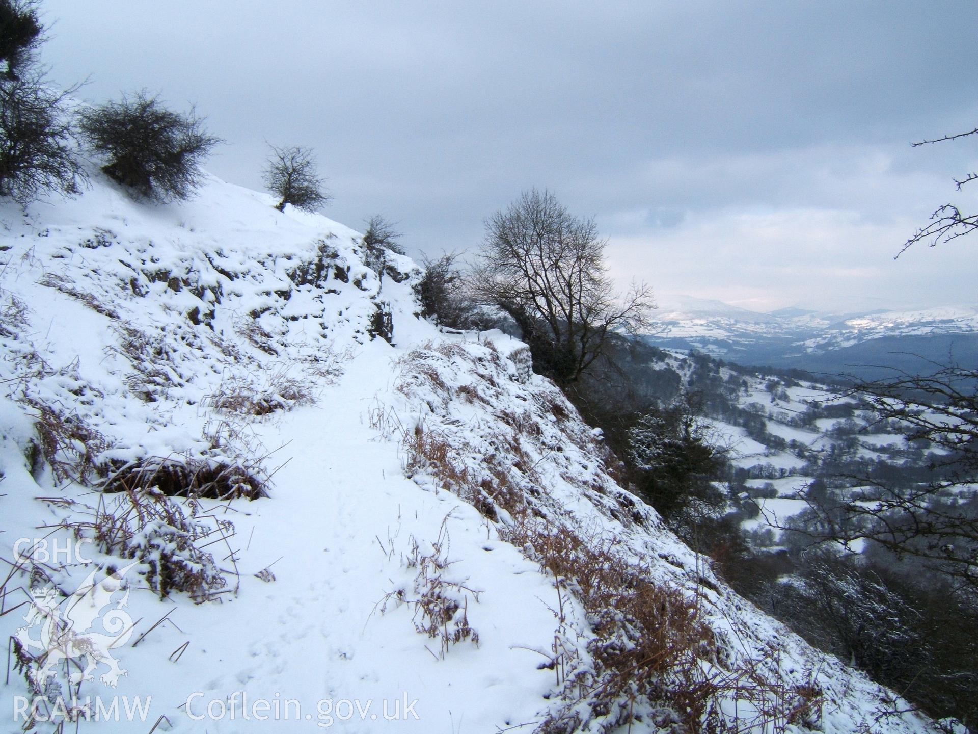 Collapsed tramroad terrace approaching fenced curve to Pwll Du Quarry from SE in snow.