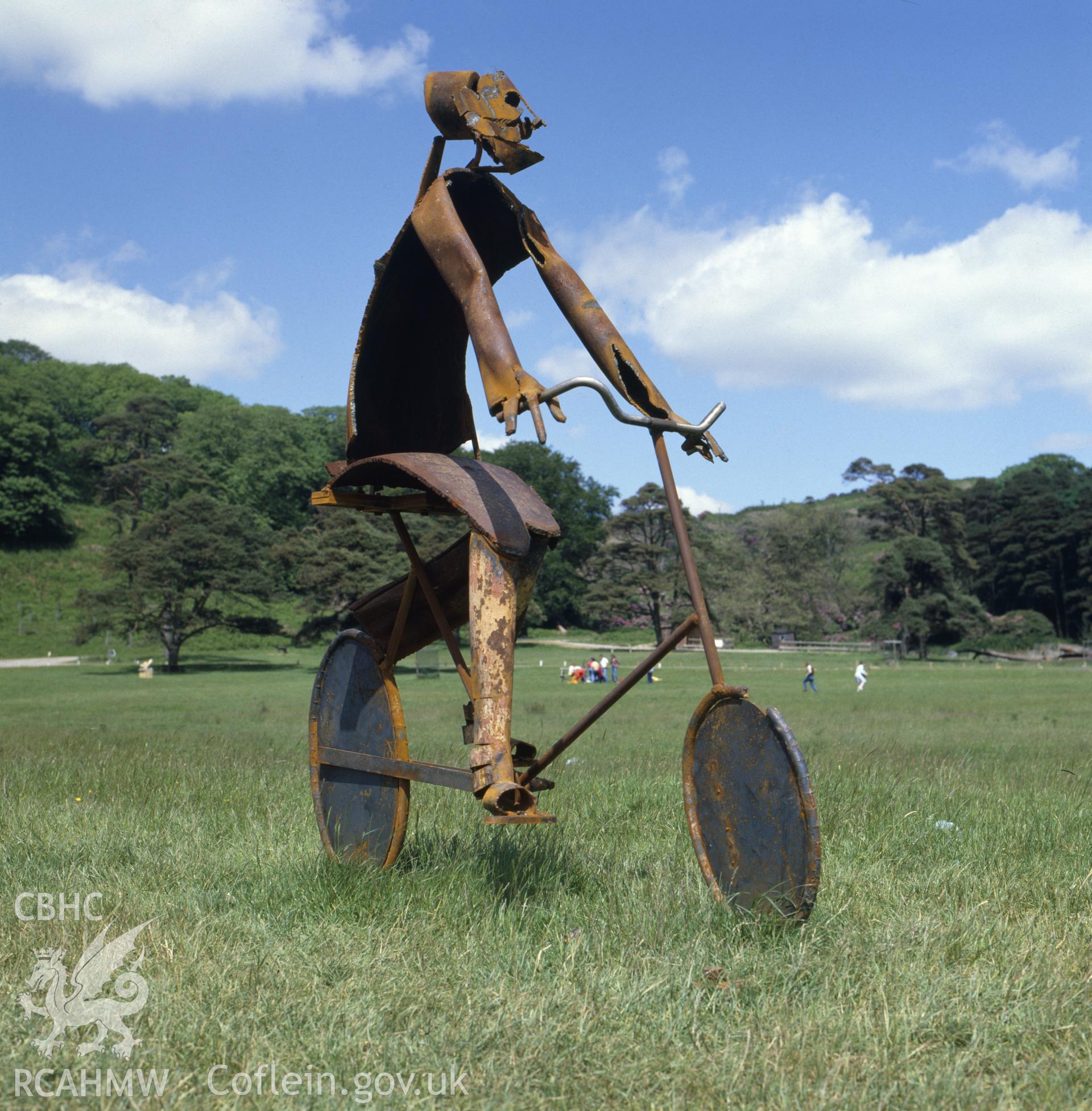 1 colour transparency showing view of sculpture enitled: 'Girl on a Bicycle' by Robert Scriven, situated at Margam sculpture park; collated by the former Central Office of Information.