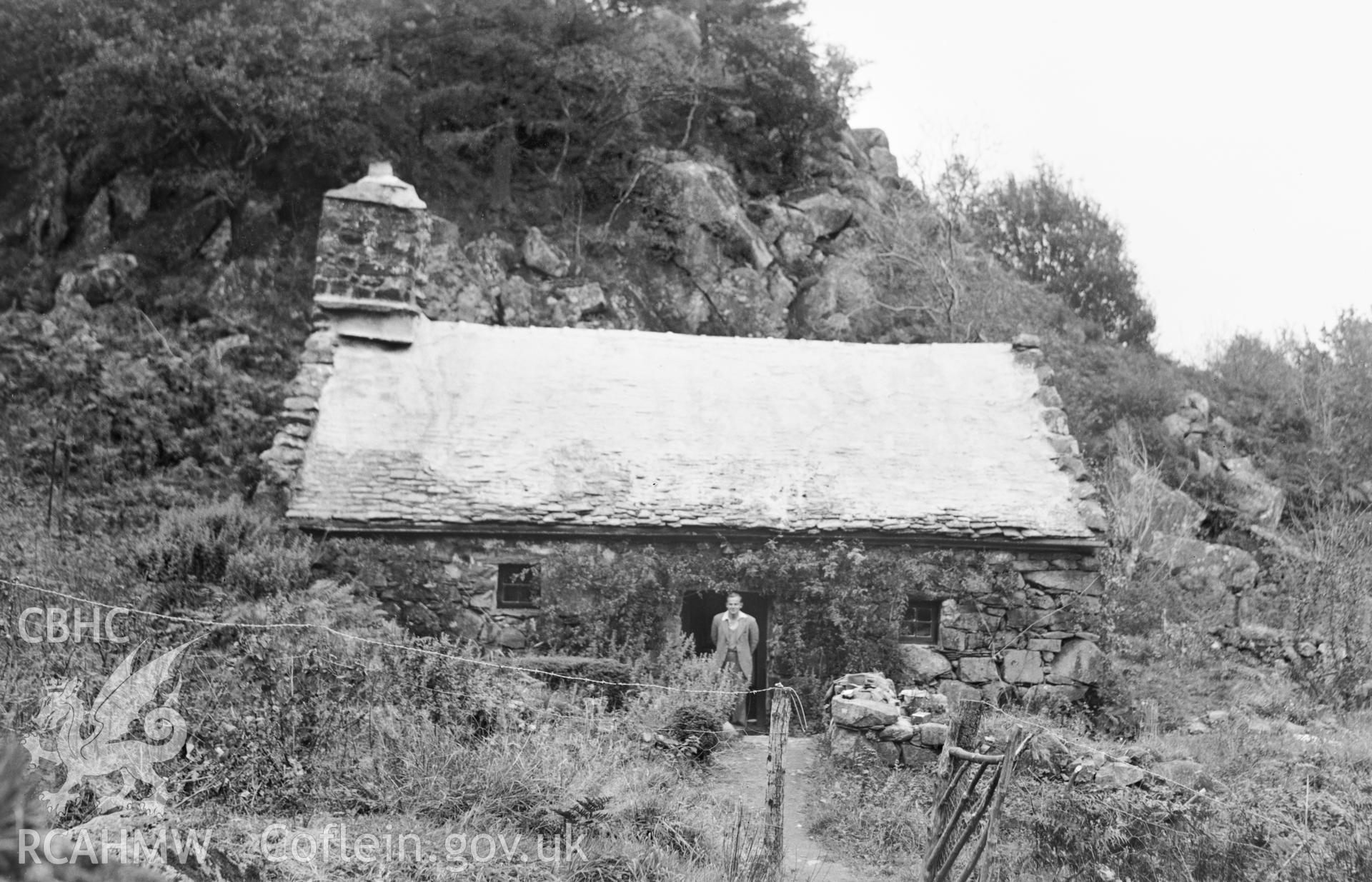 Black and white photograph of Oerddwr Isaf, Beddgelert featuring Peter Smith in the foreground, produced by RCAHMW 1953.