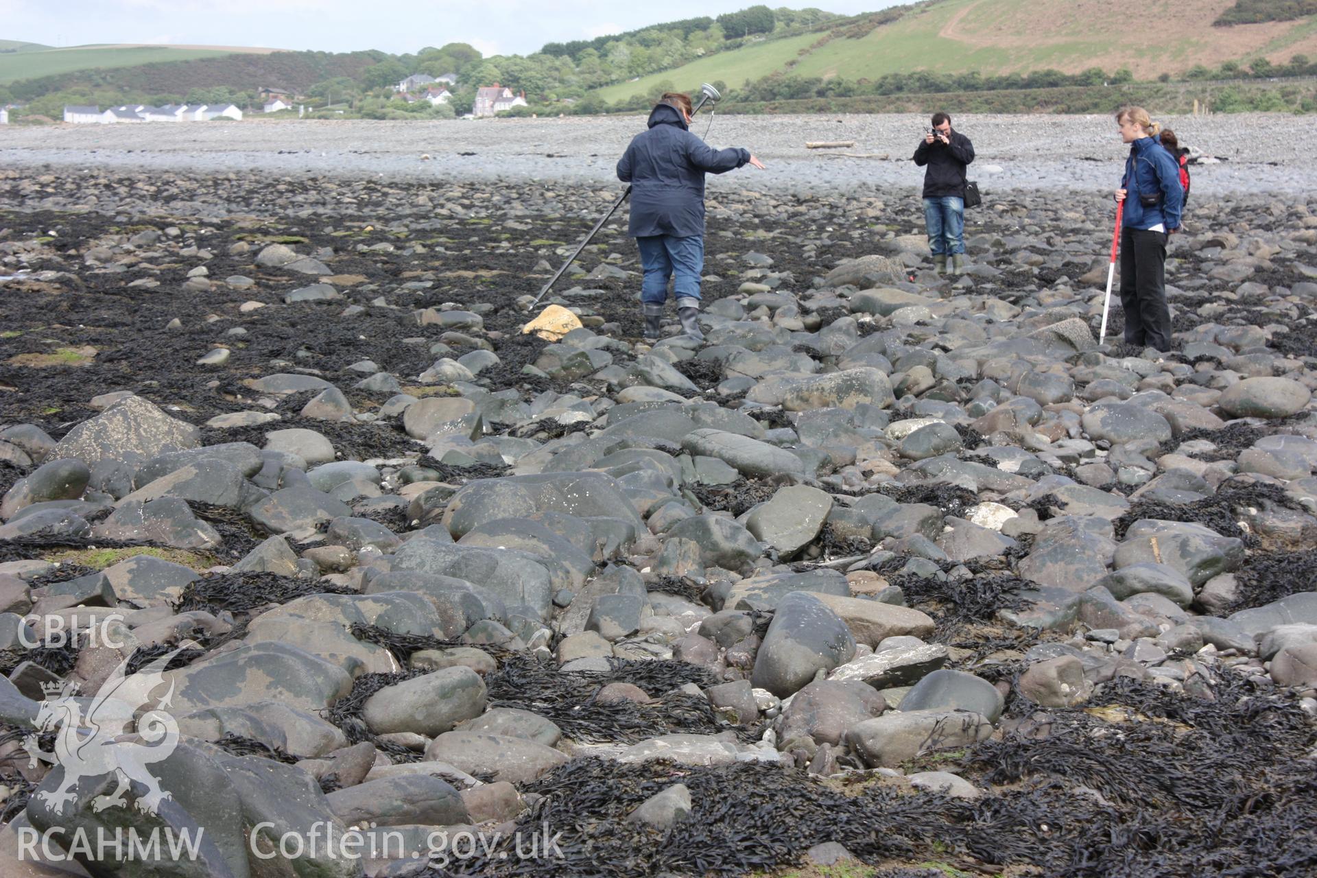 Dry stone wall comprising east-west arm of fish trap, looking east. With member of RCAHMW staff (centre) standing on line of dry stone wall, and member of RCAHMW staff and local resident showing extent of boulder spread.