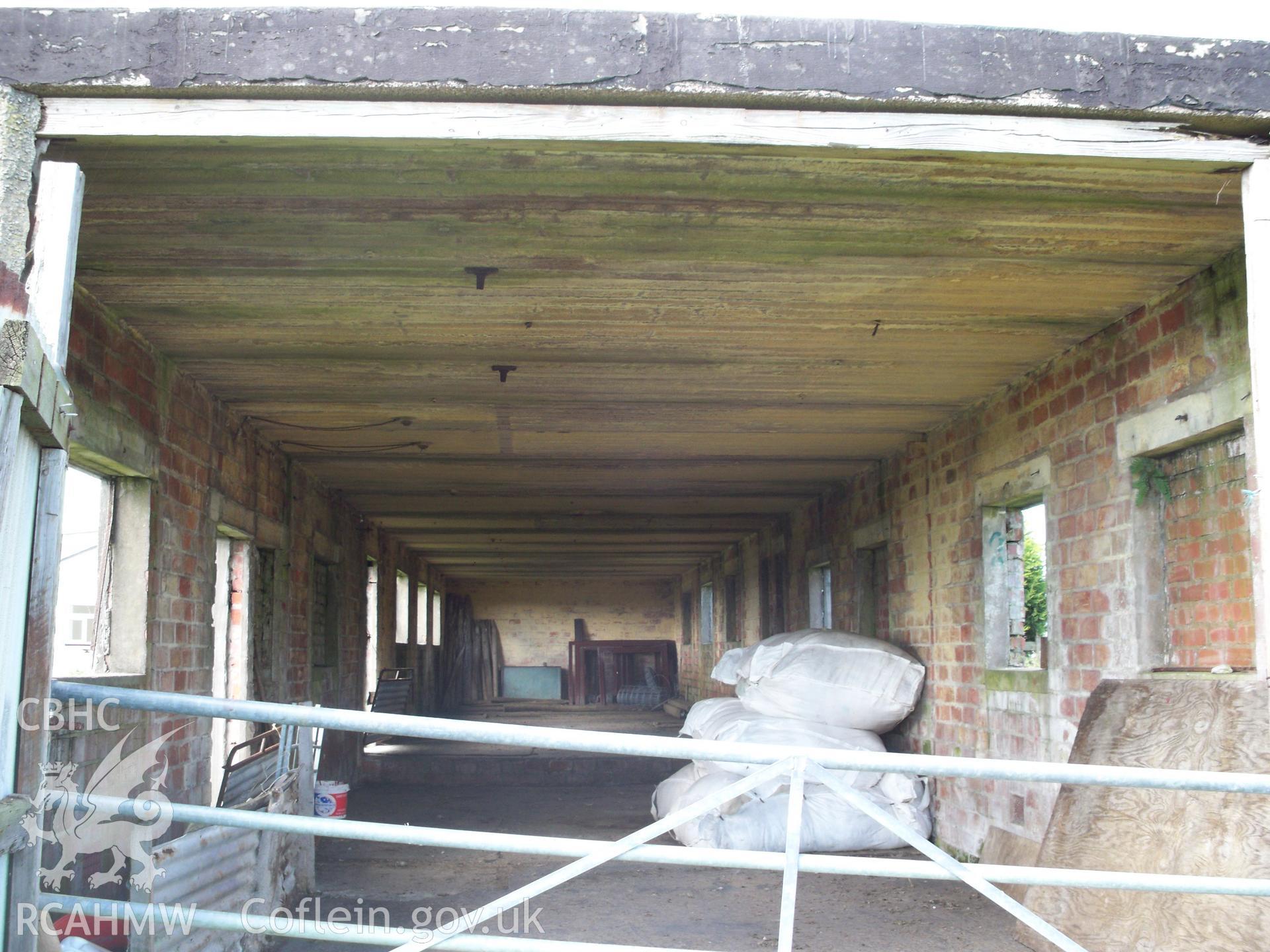 Interior of building viewed from eastern end showing concrete roof and range of windows and doors on both sides, plus step up to western end of building.