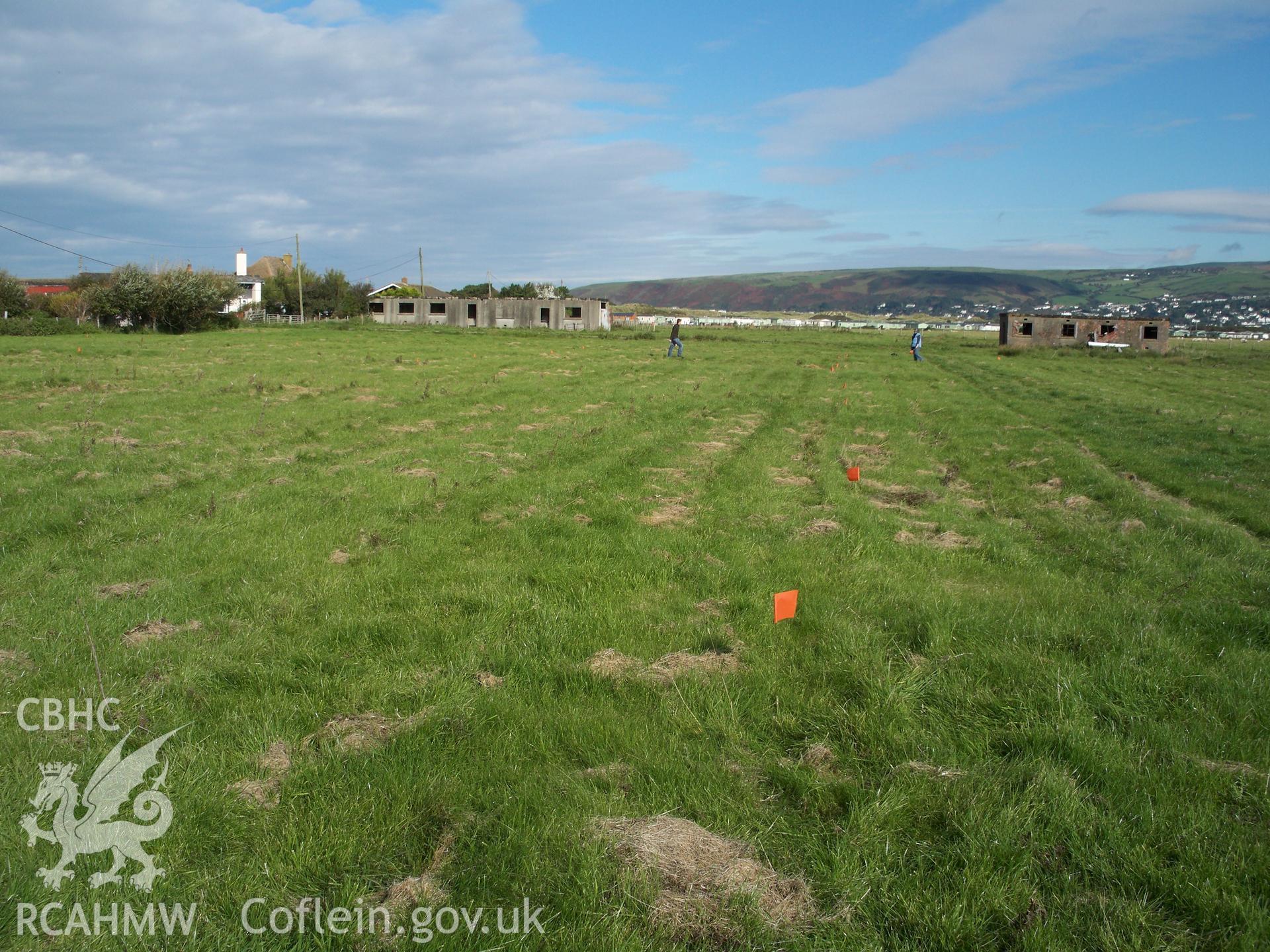 View looking north across the remaining 12 hut platforms (survey flags mark edges)