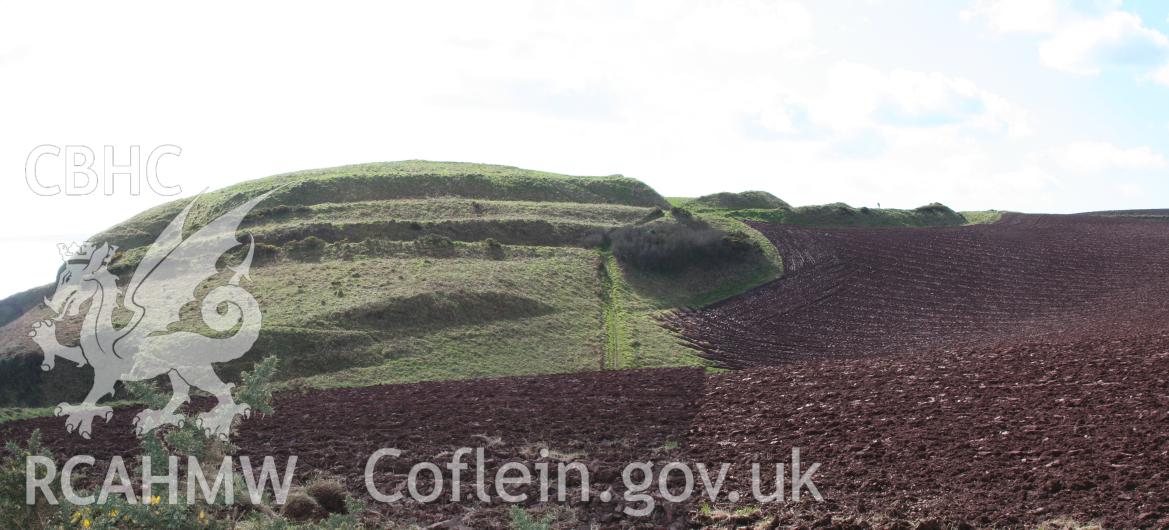 Panoramic ground view from the north showing the elevated interior of the main inner fort with the northern defences below (left), the northern outer annexe (left foreground), earthworks of the western annexe (on horizon, right, with figure for scale).