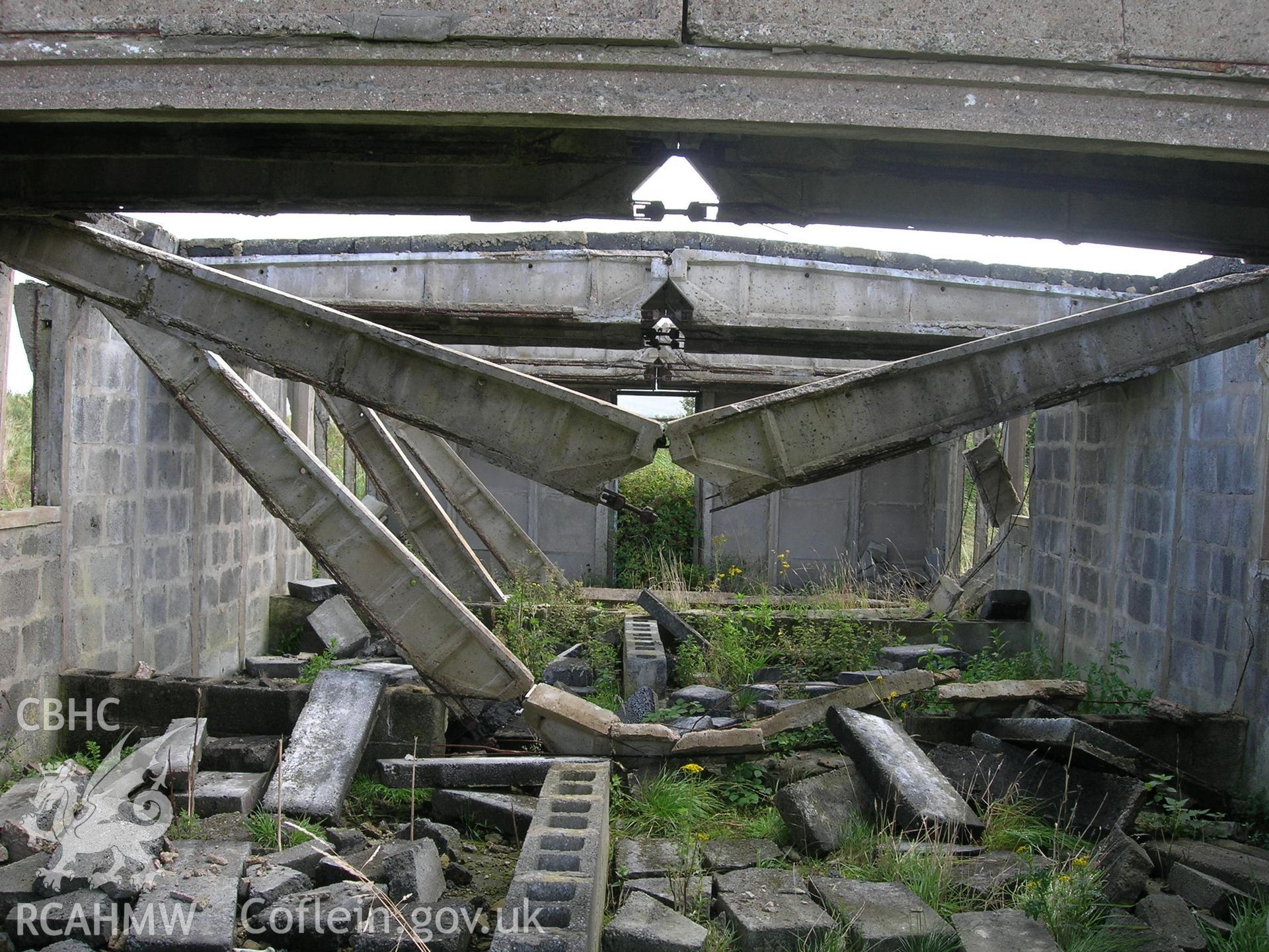 Interior of BCF hut showing collapsed roof spans and steel cable ties holding the spans together. End walls retains the original concrete panels, side walls appear to have been replaced with modern breeze blocks