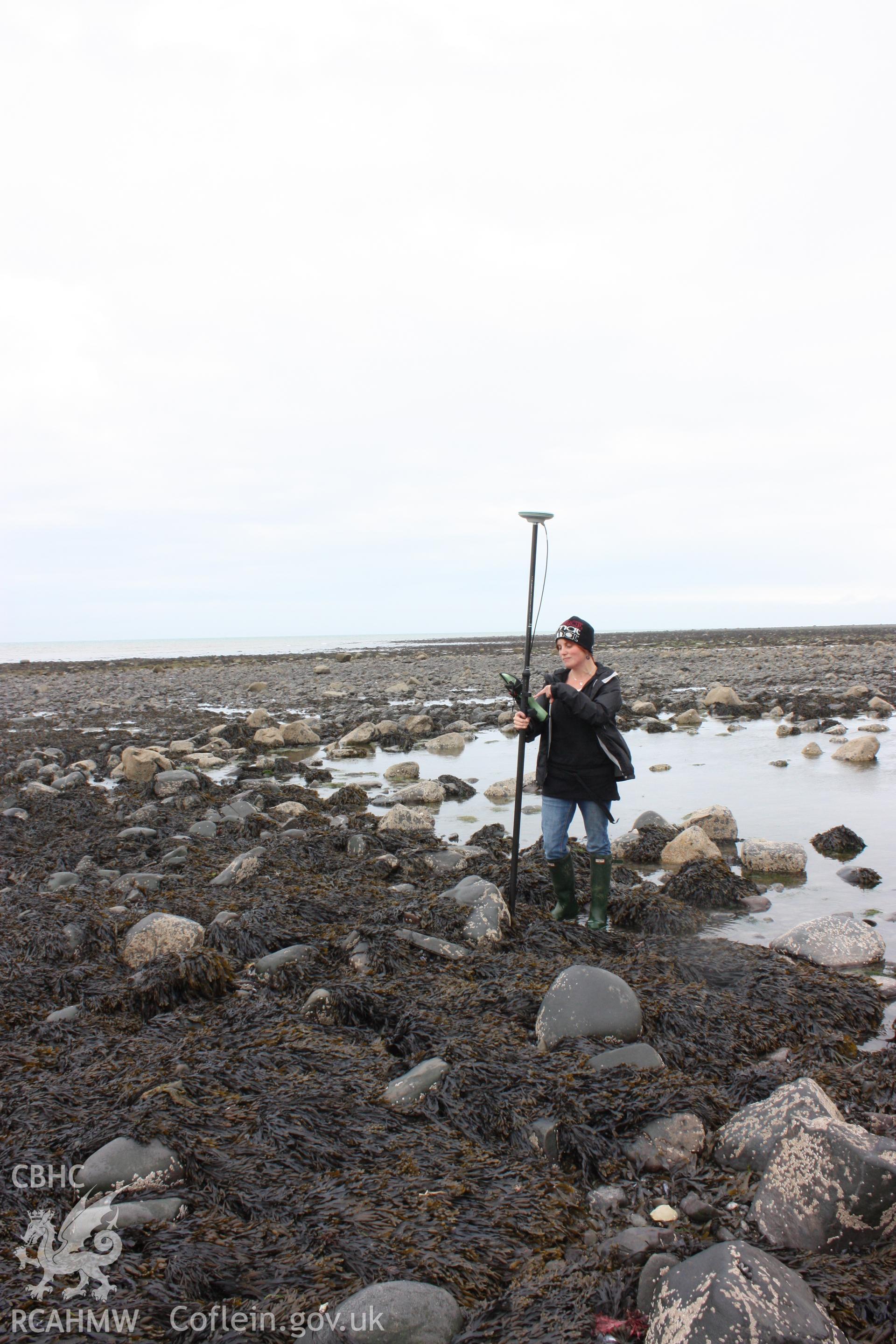 Northern section of fish trap arm, looking northwest. Shows curving alignment of boulders comprising remains of dry stone wall, with pool of water still retained by fish trap arm. RCAHMW staff member for scale.