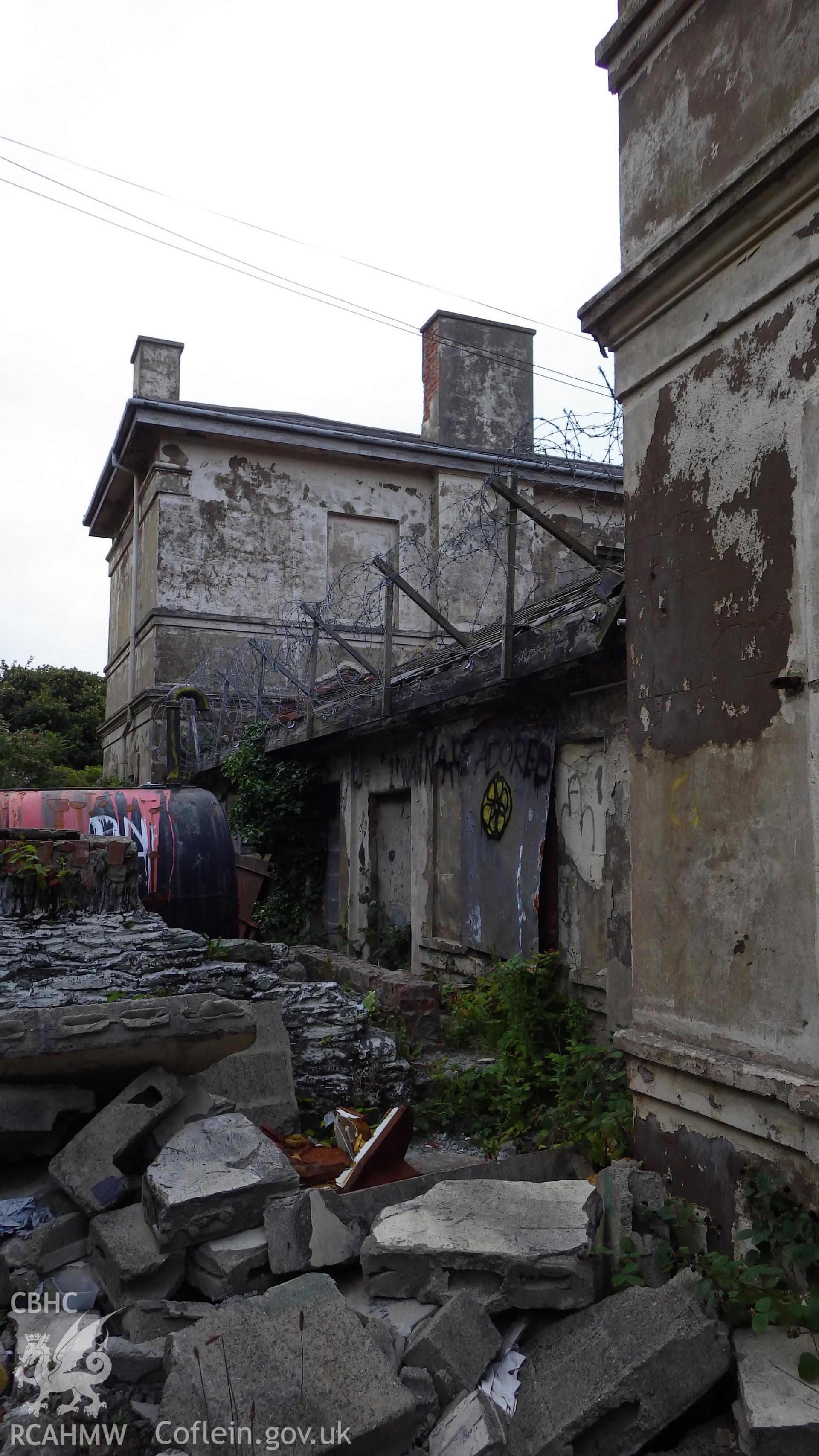 Northern wing in background, single storey infill between the two wings (barbed wire on top) and building rubble