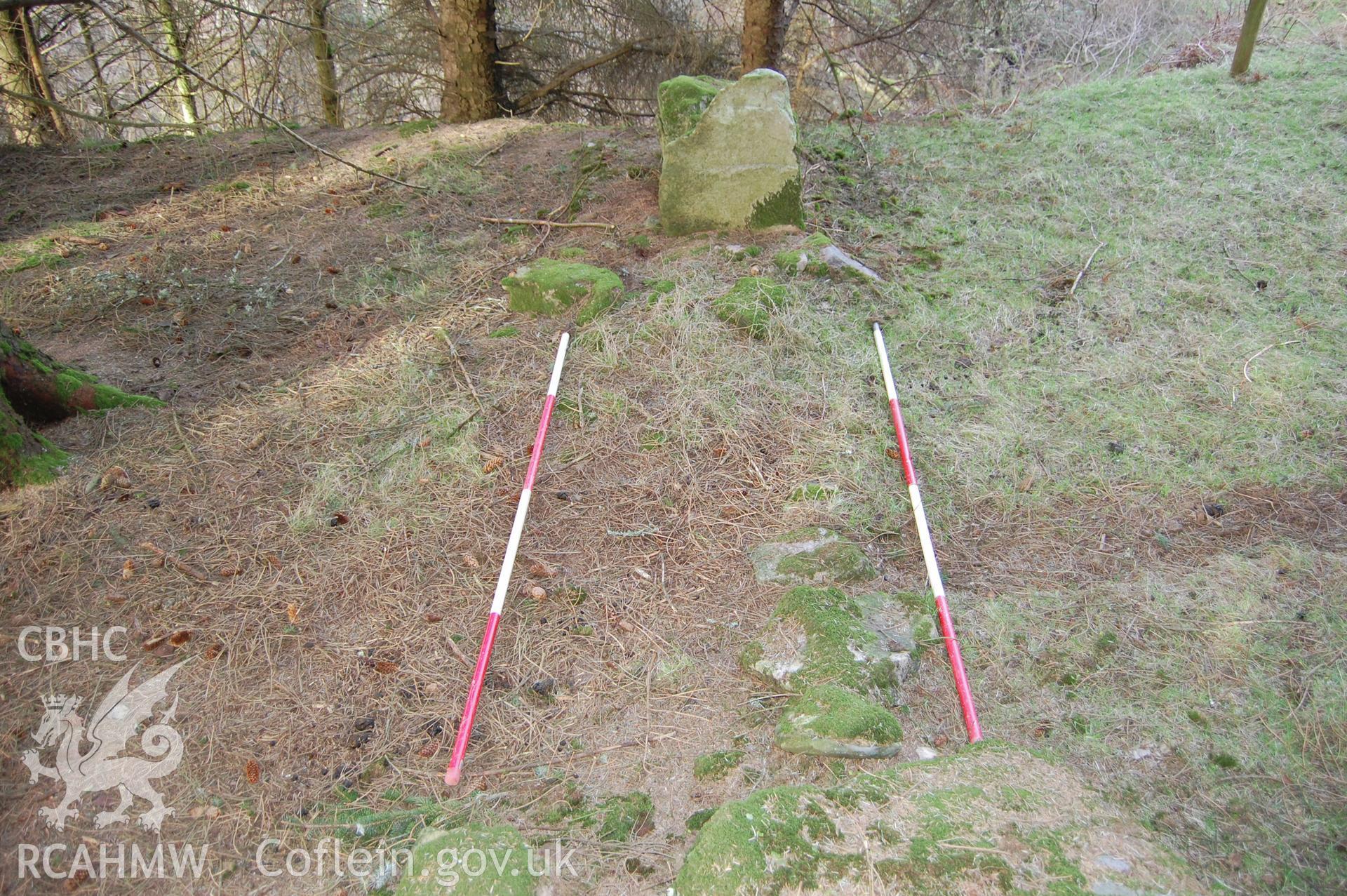 Photo showing 'View of suggested breaching point of Wall with ranging poles marking original width of Wall' from Archaeological Assessment of Nant Gwrtheyrn Lower Car Park, Nant Gwrtheyrn, Gwynedd produced by Gwynedd Archaeological Trust in 2013, Project No. G2313, Report No.1208.