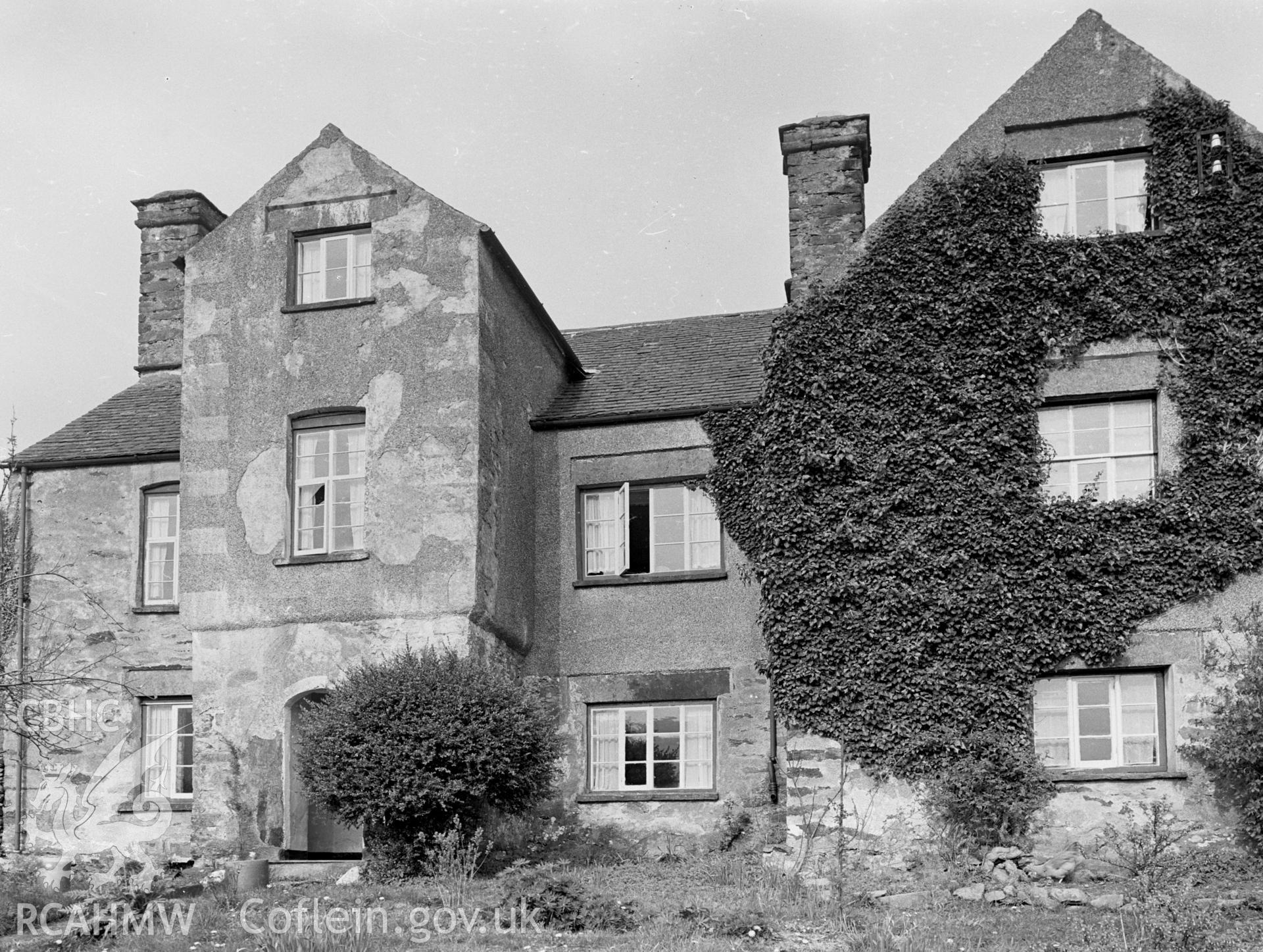 A view of a two/three storey house. Pitched slate roof. The building is made of stone. Two chimneys.