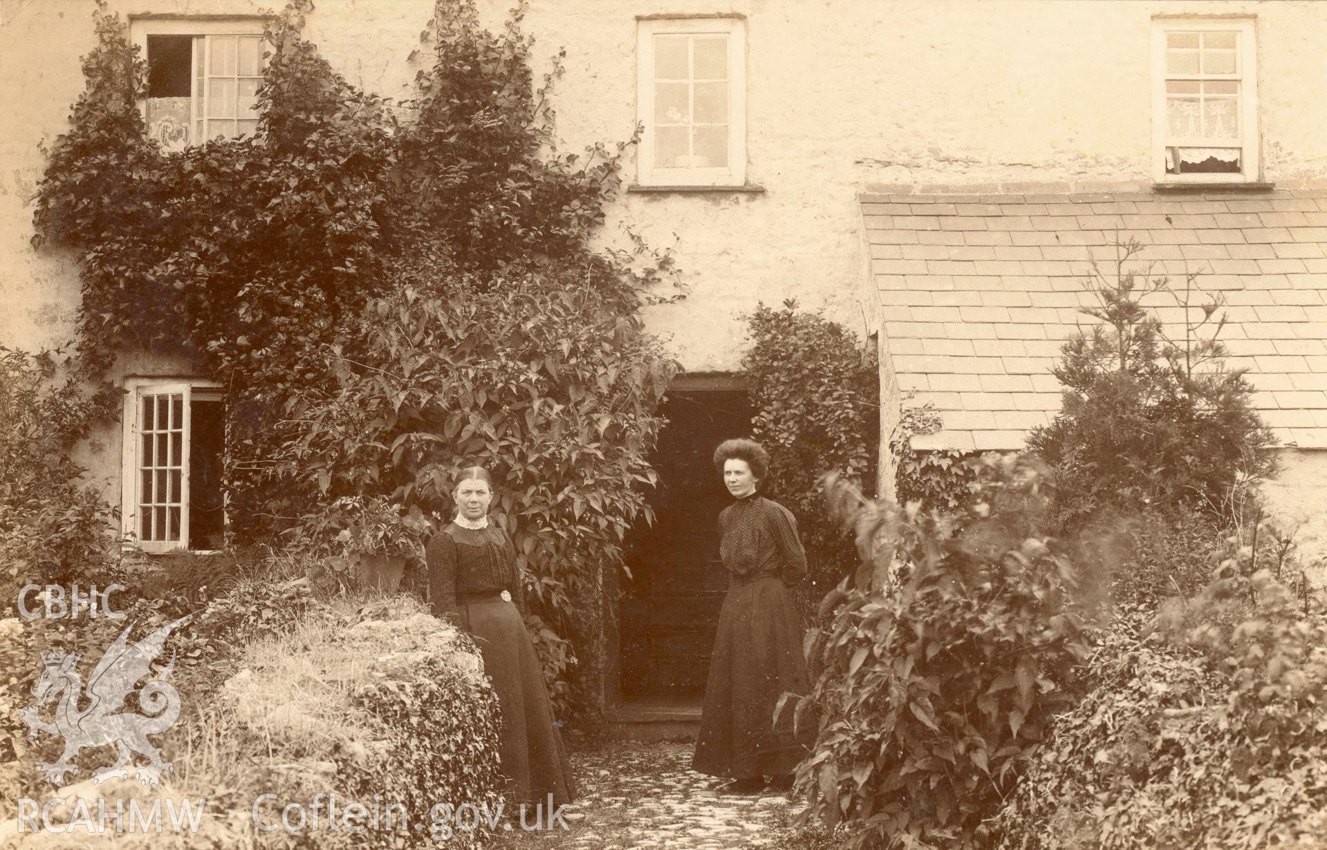 Digitised postcard image of two ladies in front of an unidentified house in Tenby, H. Mortimer Allen, Tenby. Produced by Parks and Gardens Data Services, from an original item in the Peter Davis Collection at Parks and Gardens UK. We hold only web-resolution images of this collection, suitable for viewing on screen and for research purposes only. We do not hold the original images, or publication quality scans.