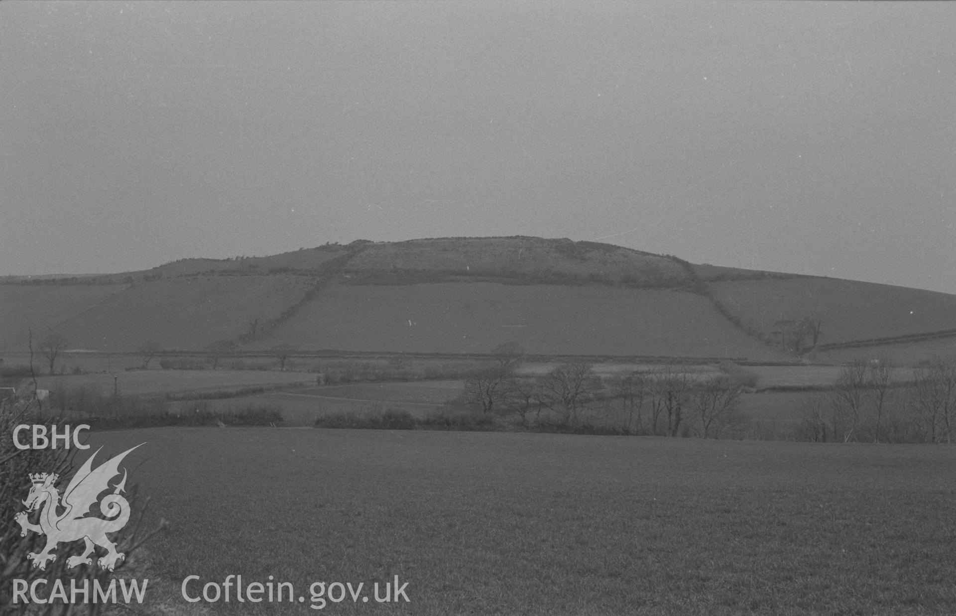 Black and White photograph showing Caer Pwll-Glas iron-age camp from the lane just east of Dolau. Photographed by Arthur Chater in April 1962 from Grid Reference SN 639 862, looking north west.