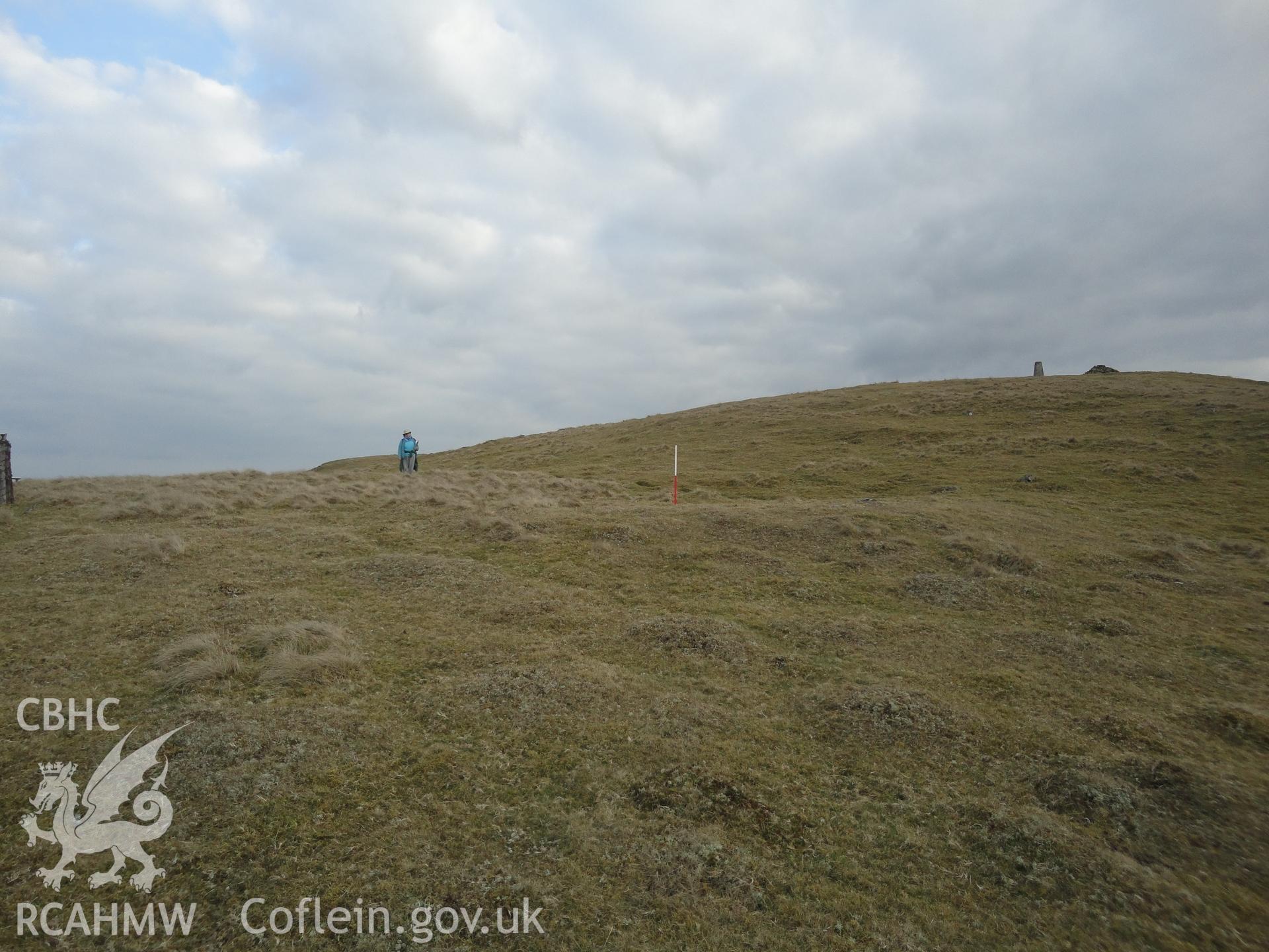 Hut platform in the background on which the person is standing with NPRN 511878 in the foreground, looking south.