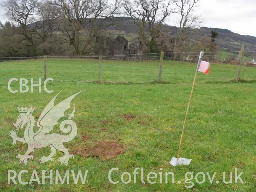 Digital colour photograph of Grosmont battlefield, with Grosmont Castle in the distance, partially hidden by trees. From report no. 1049 - Grosmont battlefield, part of the Welsh Battlefield Metal Detector Survey, carried out by Archaeology Wales.