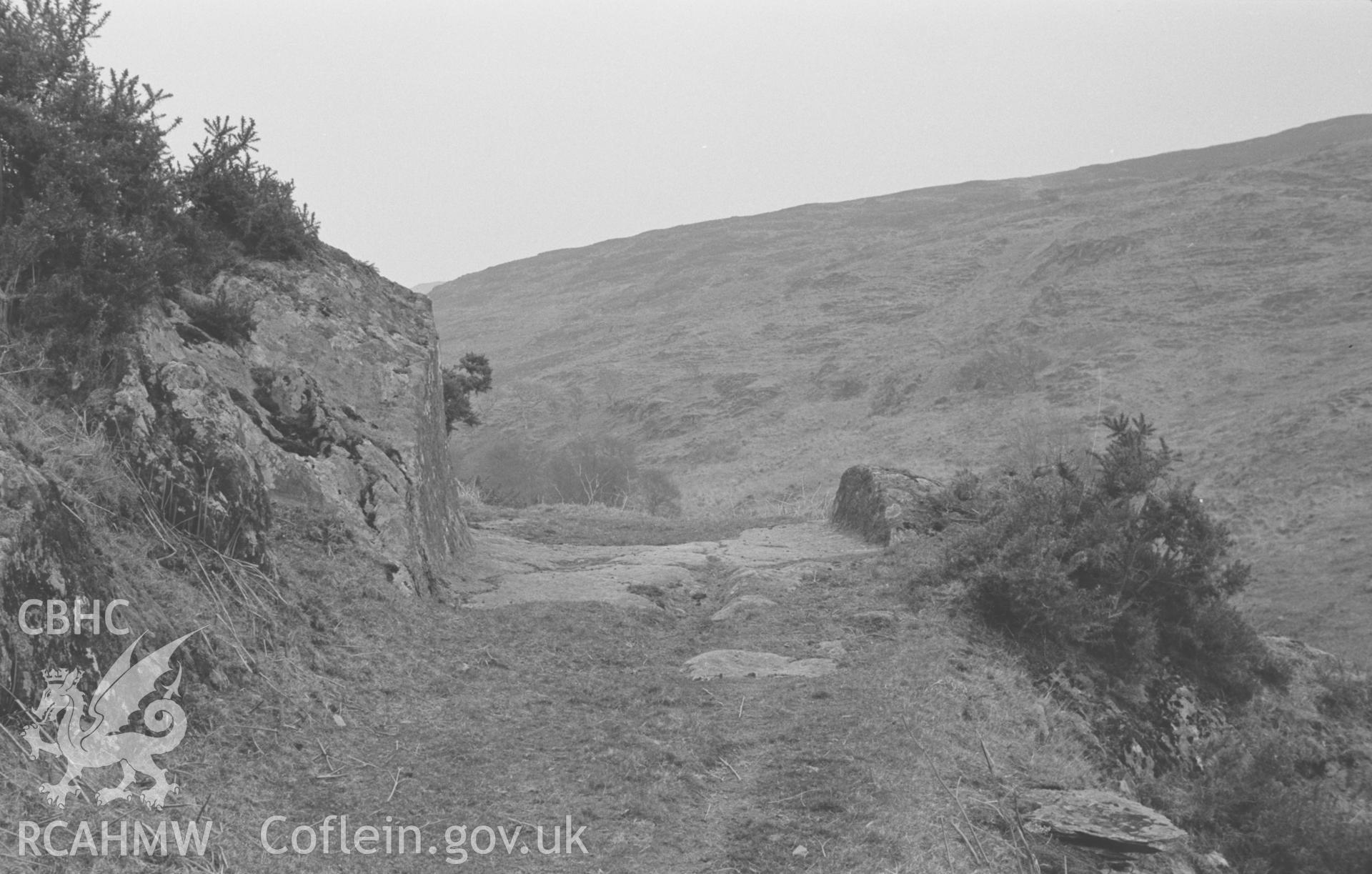 Digital copy of a black and white negative showing view up the Afon Brwyno valley c.400m above Brwyno, showing road from Brwyno to Brwyno-Canol and Brwyno-Uchaf cut through rock. Photographed in March 1964 by Arthur O. Chater.