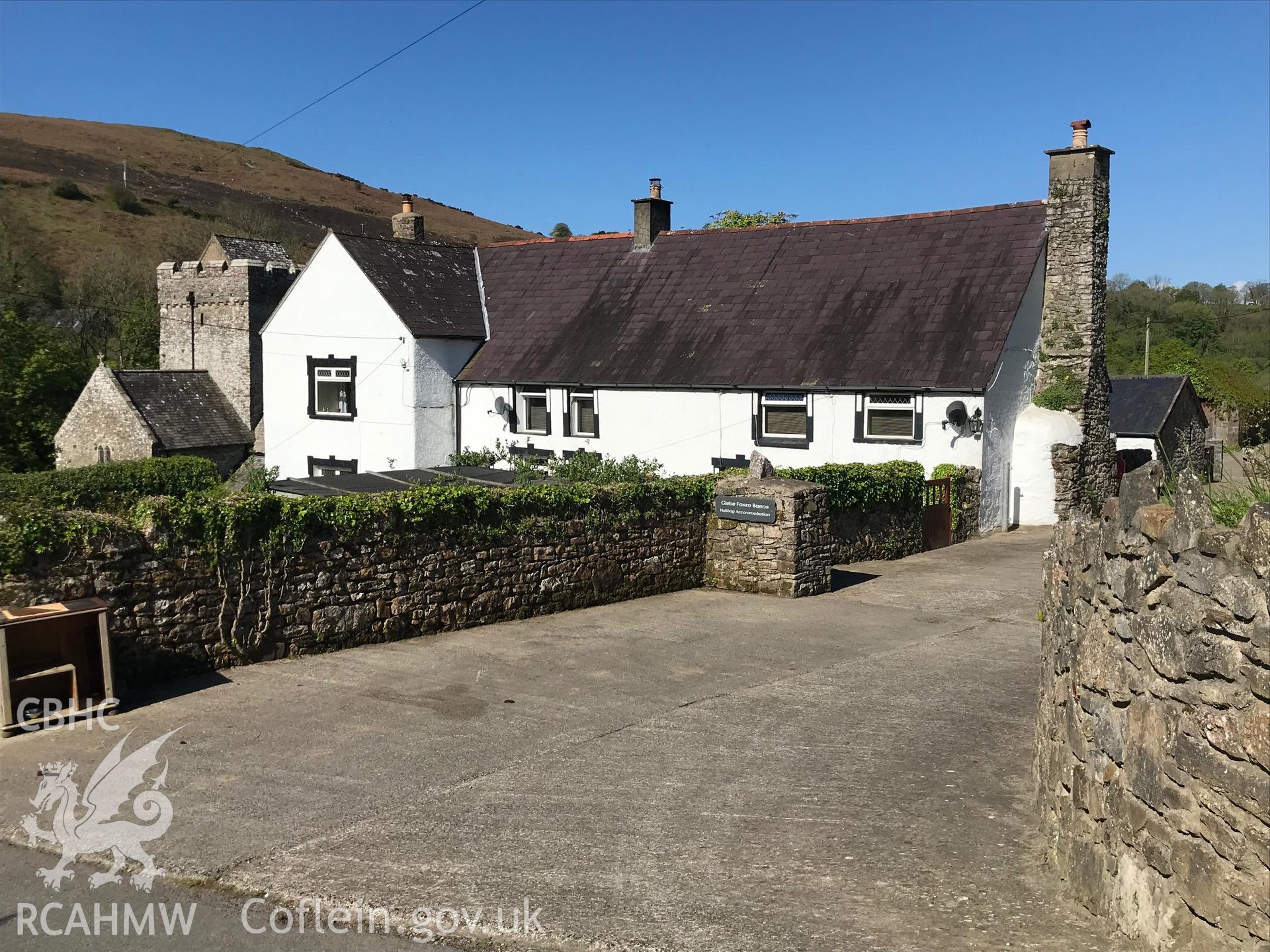 Digital colour photograph showing exterior view of Glebe farmhouse, Cheriton, Llangennith, with St. Cadog's church in the background, taken by Paul R. Davis on 5th May 2019.