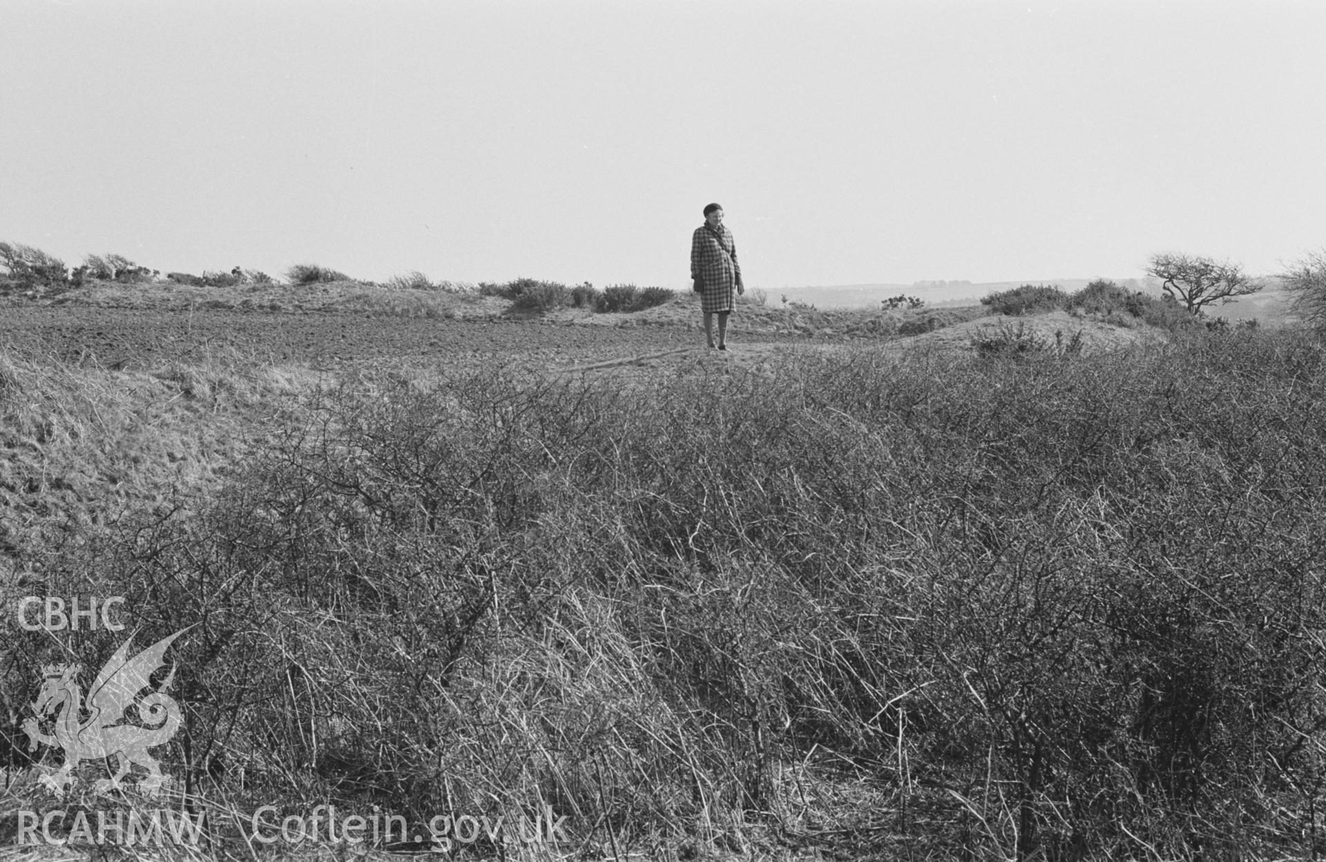 Digital copy of a black and white negative showing The Castell; looking across the west and south ramparts (with woman). Photographed by Arthur O. Chater in April 1968. (Looking south east from Grid Reference SN 355 555).