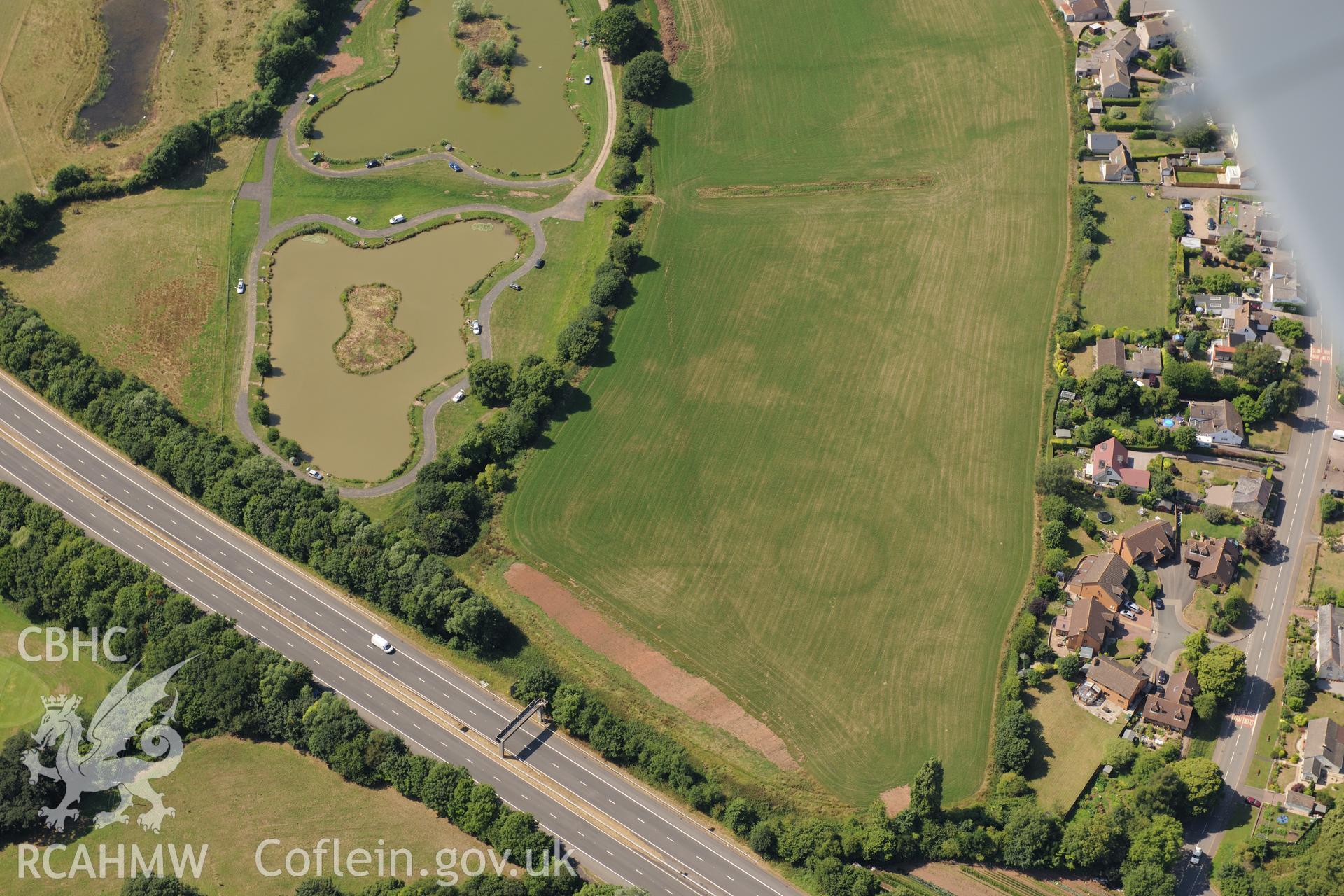 Round barrow cropmarks and the village of Newton Green,south west of Chepstow, with the M48 passing to the south. Oblique aerial photograph taken during the Royal Commission?s programme of archaeological aerial reconnaissance by Toby Driver on 1st August