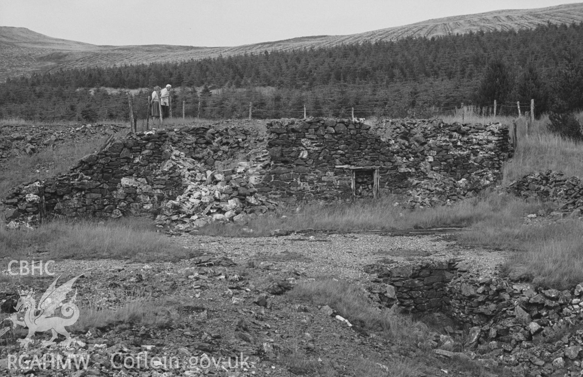 Digital copy of a black and white negative showing ruin of building just north of the reservoir at Esgair Fraith lead mine (with figures). Photographed by Arthur O. Chater on 22nd August 1967 looking north from Grid Reference SN 739 914.