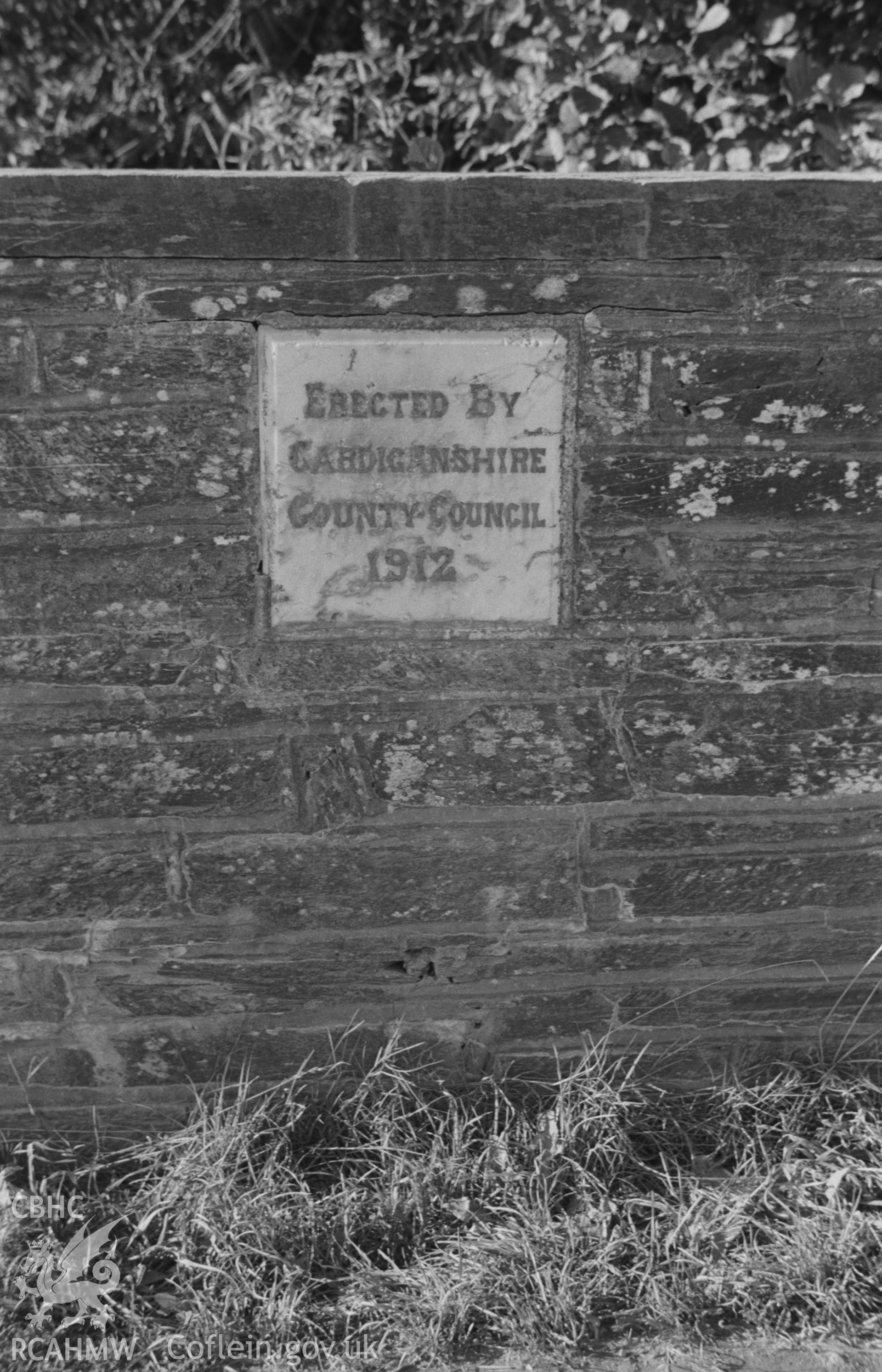 Digital copy of a black and white negative showing inscription on roadside marble plaque on stone wall, dated 1912, on north side of the Llandygwydd road opposite Glanarberth, Llechryd. Photographed by Arthur O. Chater on 11th September 1964.