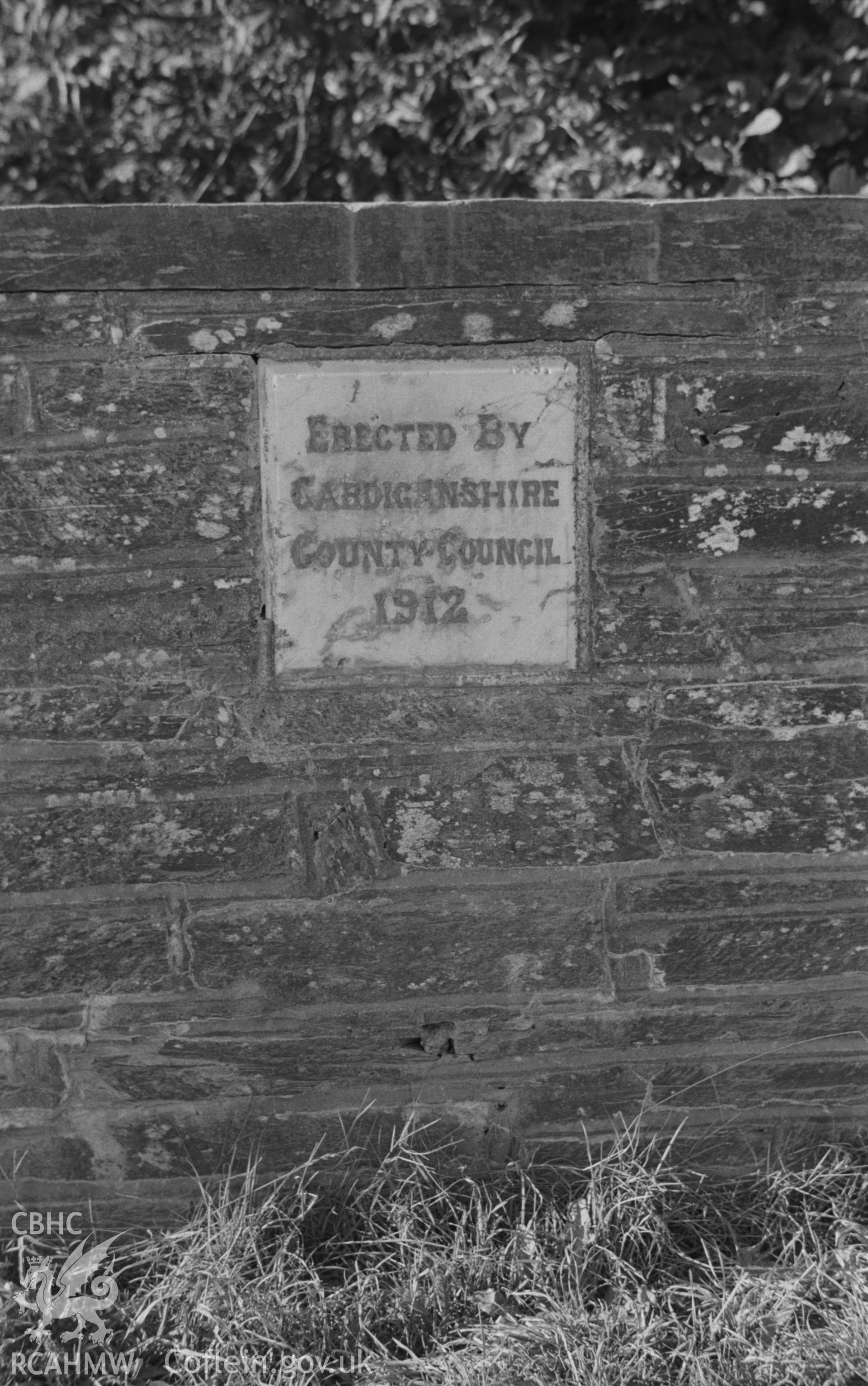 Digital copy of a black and white negative showing inscription on roadside marble plaque on stone wall, dated 1912, on north side of the Llandygwydd road opposite Glanarberth, Llechryd. Photographed by Arthur O. Chater on 11th September 1964.