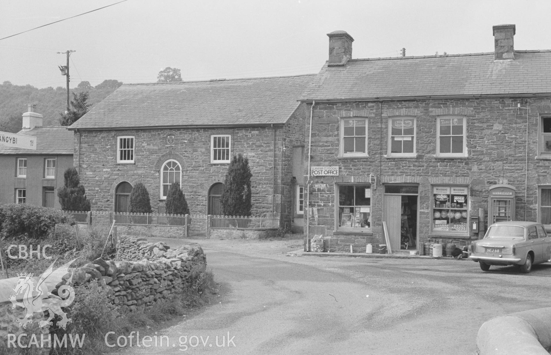 Digital copy of black & white negative showing Llanfair Clydogau post office and shop, with Capel Mair Welsh Independent chapel. Photographed by Arthur O. Chater in August 1965 from the end of Pont Llanfair. Grid Ref SN 6222 5140, looking west north west.