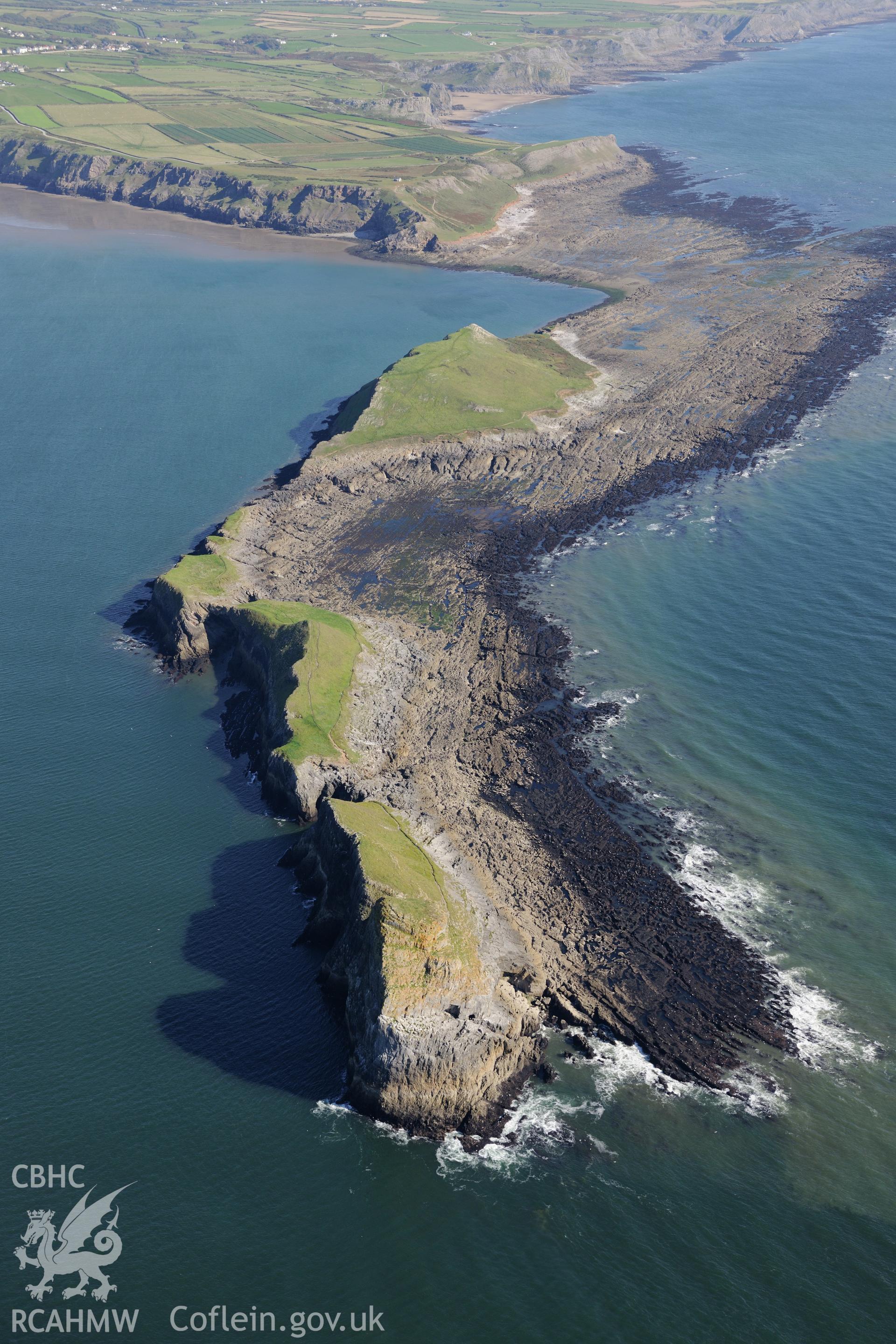 Worms Head, with Worms Head Cave in the foreground and Worm sound at low tide beyond. Oblique aerial photograph taken during the Royal Commission's programme of archaeological aerial reconnaissance by Toby Driver on 30th September 2015.