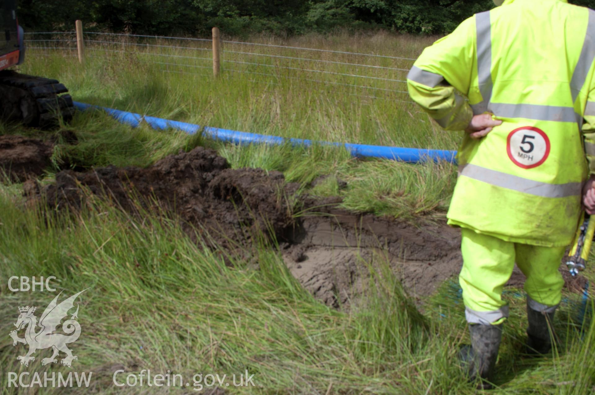 General view from north east of launch pit 2 during excavation showing grey clay below juncus. Photographed during Gwynedd Archaeological Trust's archaeological watching brief of water main renewal in Dolgellau on 28/07/2017. Project no. G2528.