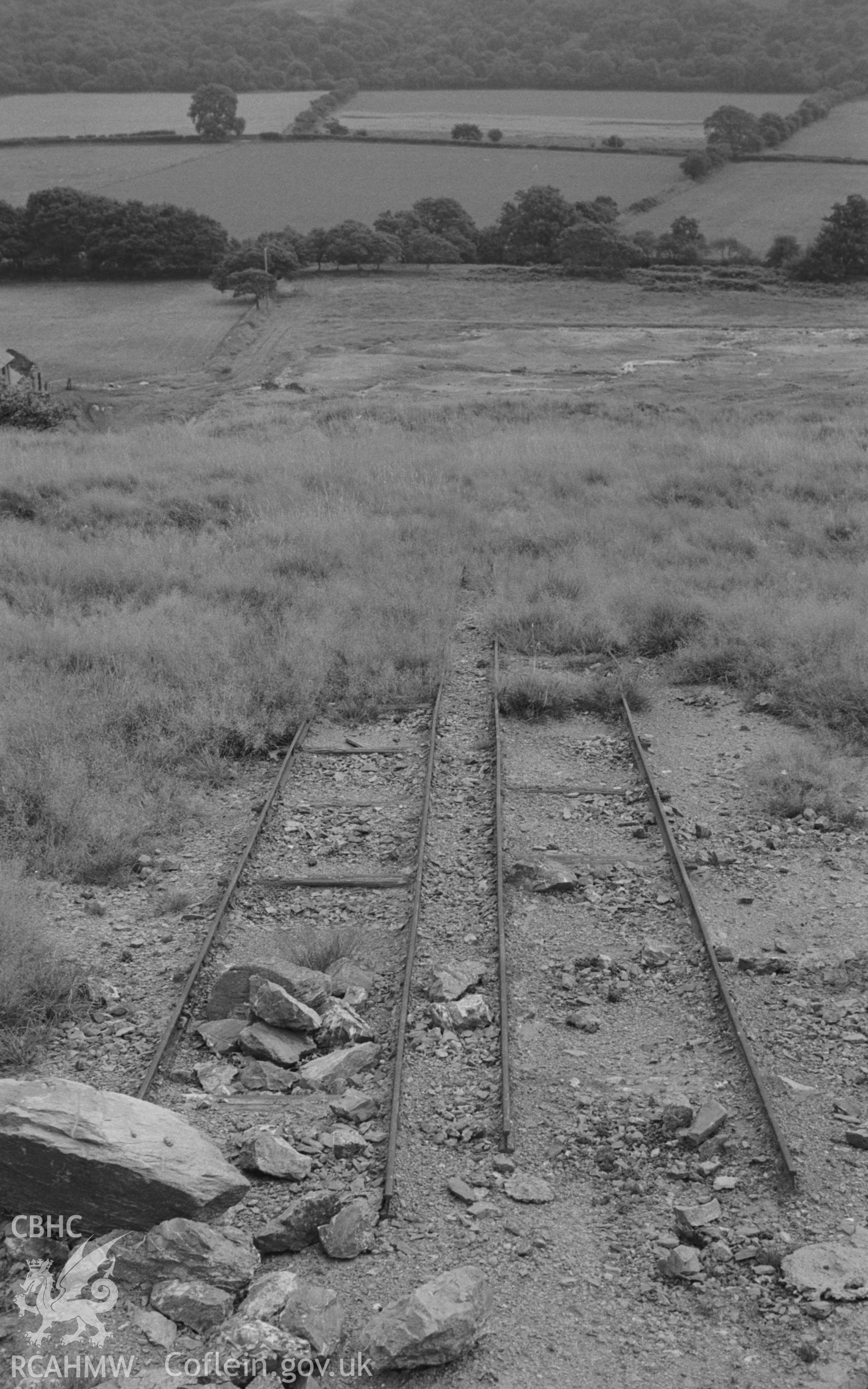 Digital copy of a black and white negative showing railway lines between the shafts and the wheel pit (and other ruins) of Abbey Consols mine. Photographed by Arthur O. Chater on 25th August 1967, looking south from Grid Reference SN 743 662.