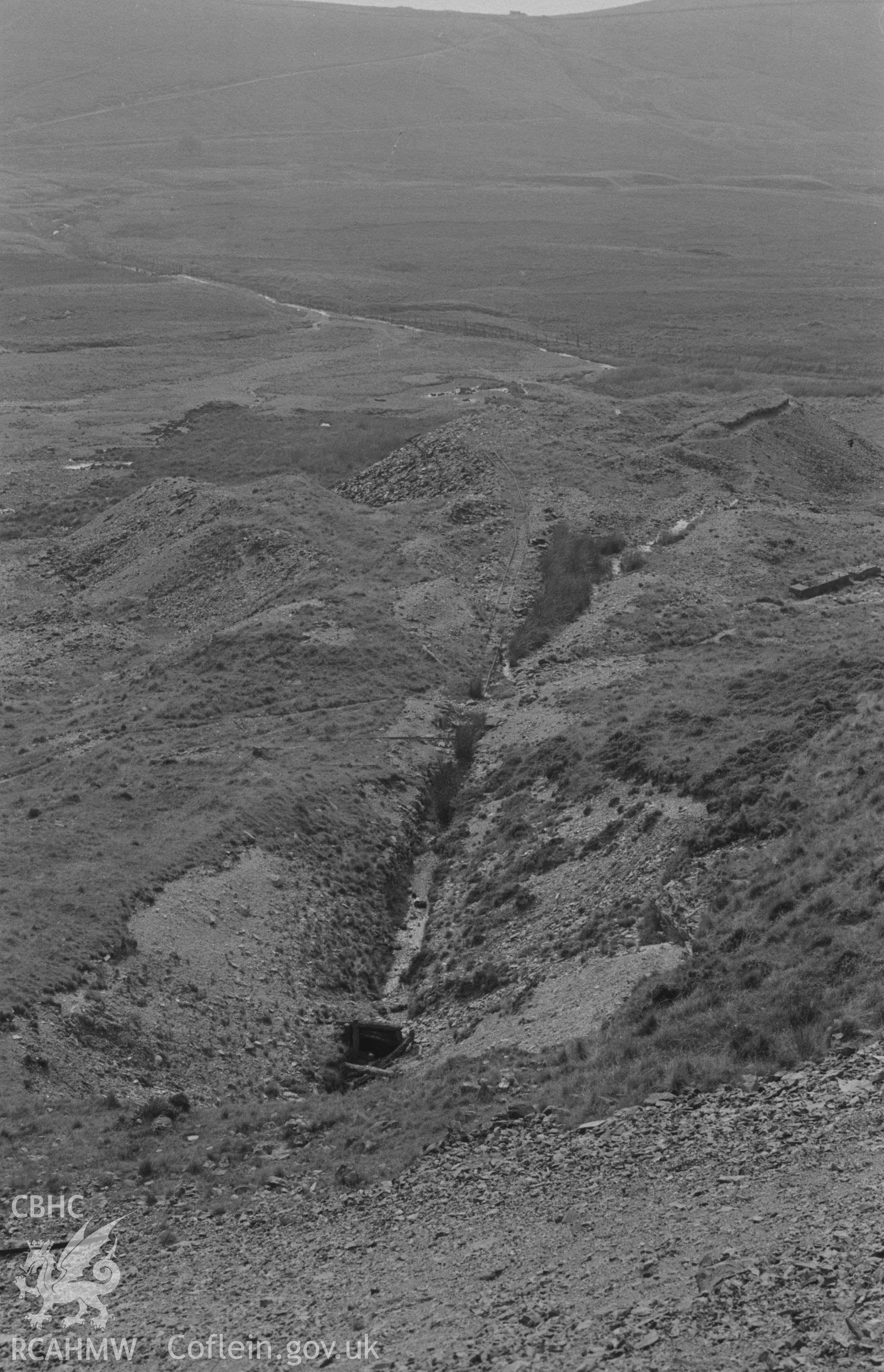 Digital copy of a black and white negative showing view down tramway leading from shaft to tips at Esgair Mwyn Mine, Ystrad Fflur. Photographed by Arthur O. Chater on 28th August 1966 looking south east from Grid Reference SN 755 691.