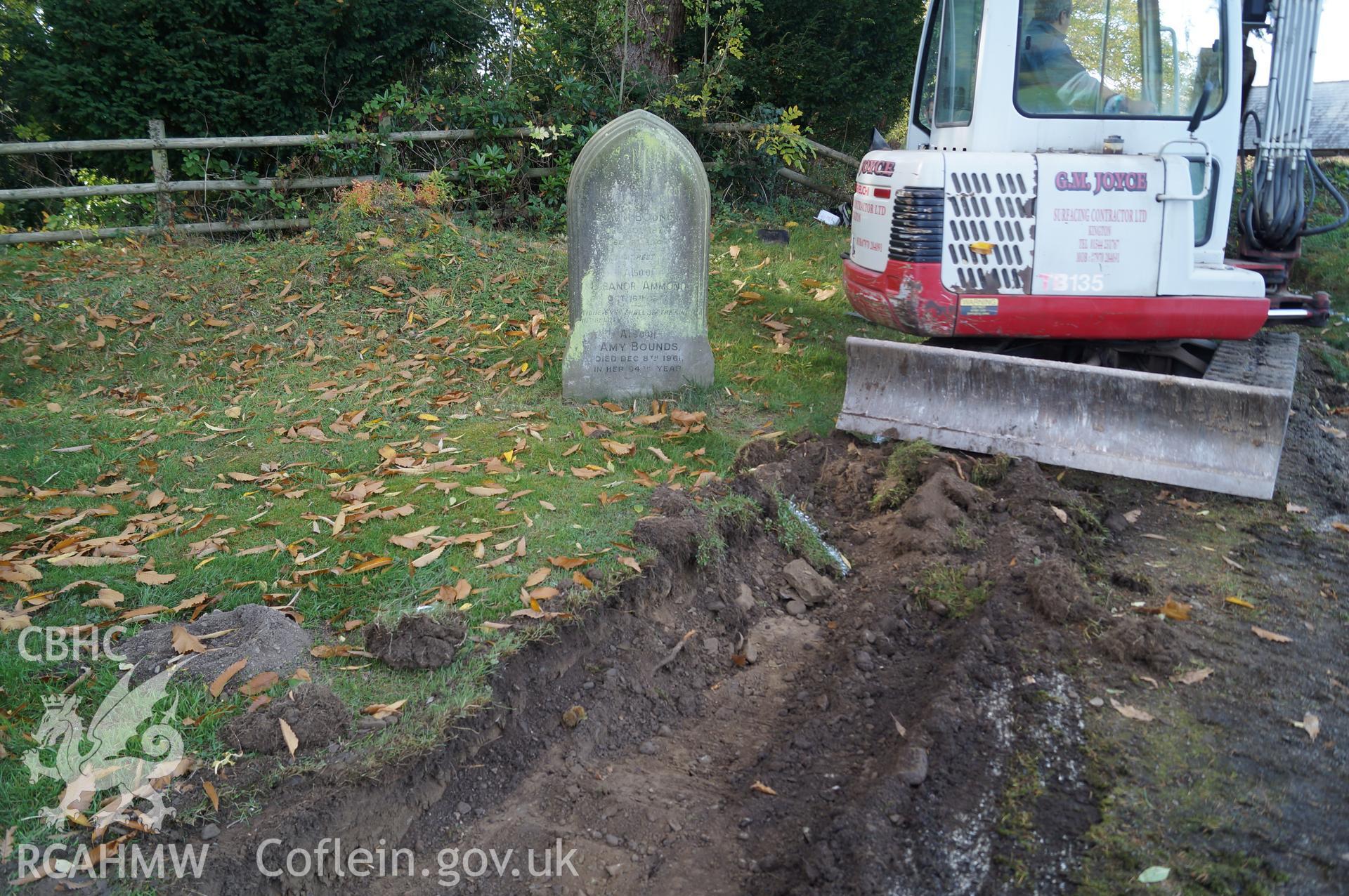 View 'looking west at excavated Trench B, on southwestern side of path, showing apparent upper fill of grave, possibly part of family associated with adjacent gravestone.' Photograph & description by Jenny Hall & Paul Sambrook of Trysor, 16/10/2017.