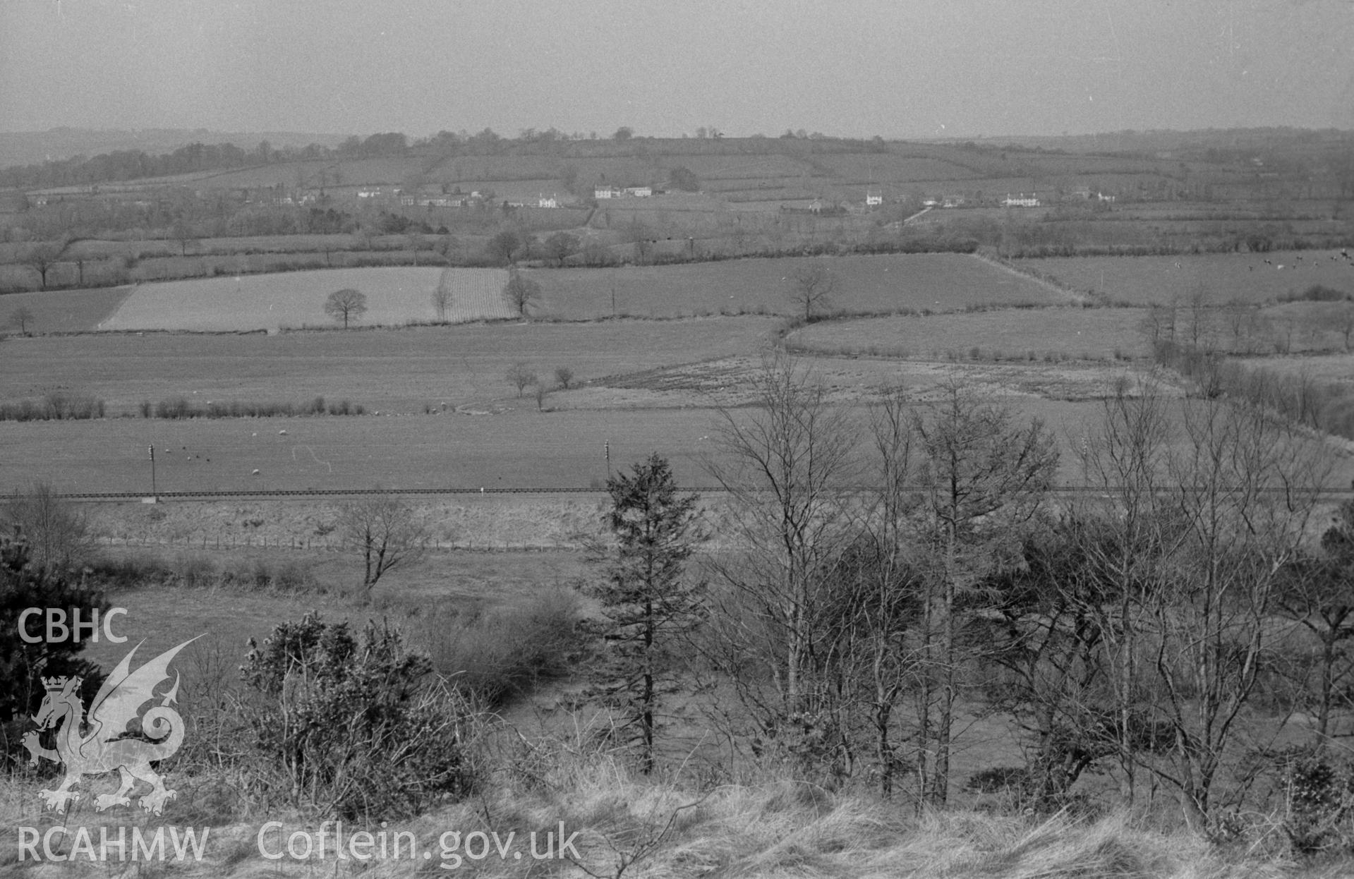 Digital copy of a black and white negative showing view from outside Pencarreg churchyard across the railway line to Alltyblaca village in the distance. Photographed by Arthur O. Chater in April 1967 looking west north west from Grid Reference SN 534 450.