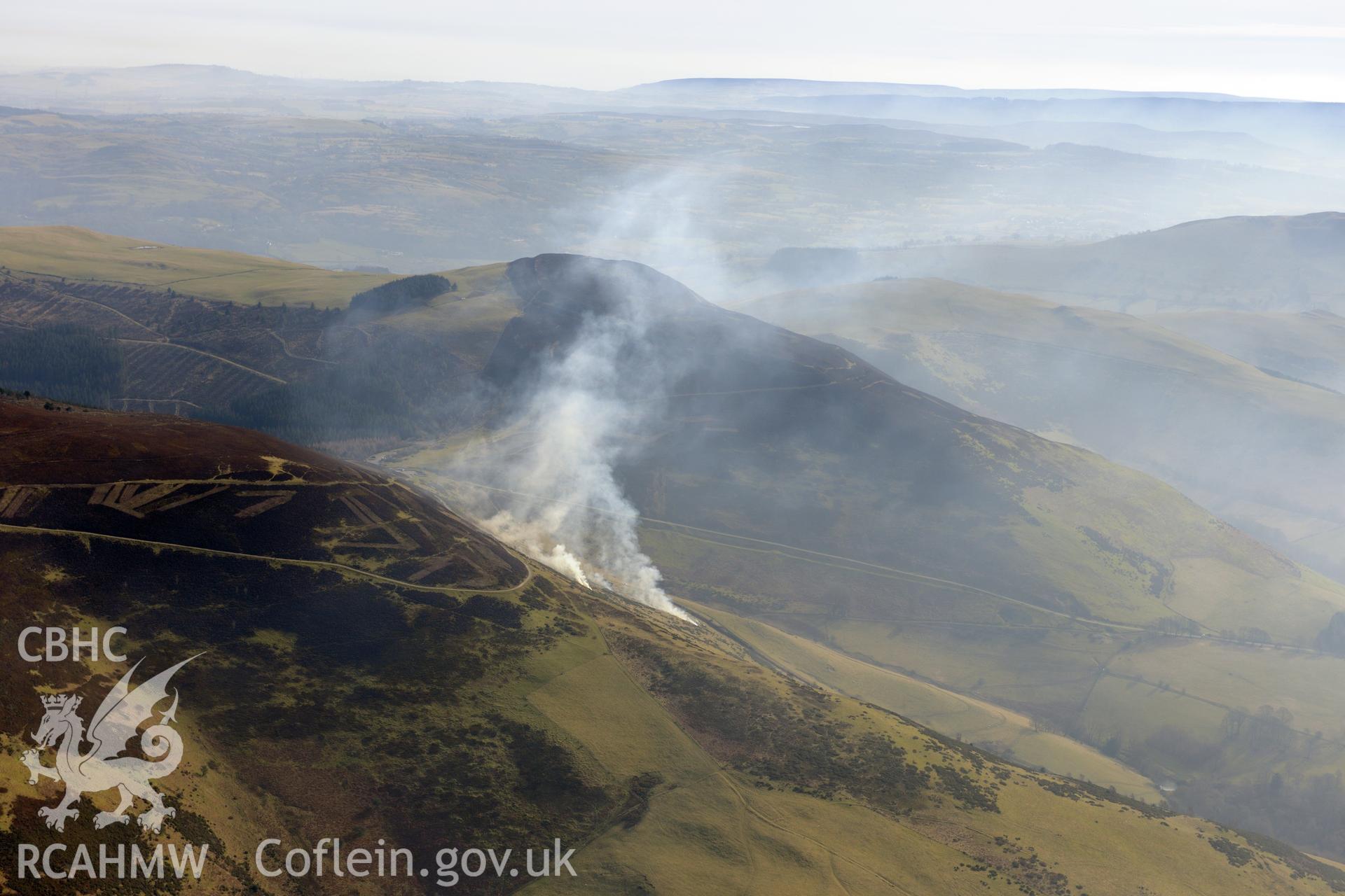 Controlled burning on moorland, with Foel Fenlli Hillfort in middle distance, between Ruthin and Mold. Oblique aerial photograph taken during the Royal Commission?s programme of archaeological aerial reconnaissance by Toby Driver on 28th February 2013.