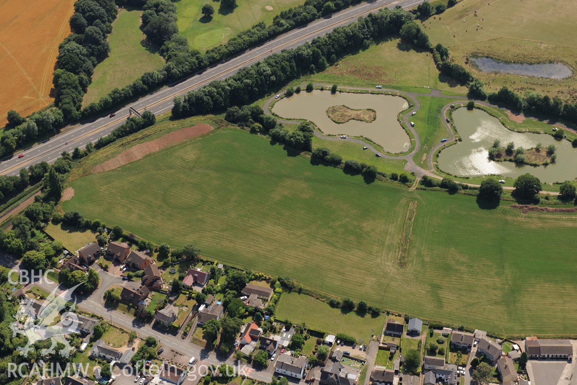 Round barrow cropmarks and the village of Newton Green,south west of Chepstow, with the M48 passing to the south. Oblique aerial photograph taken during the Royal Commission?s programme of archaeological aerial reconnaissance by Toby Driver on 1st August