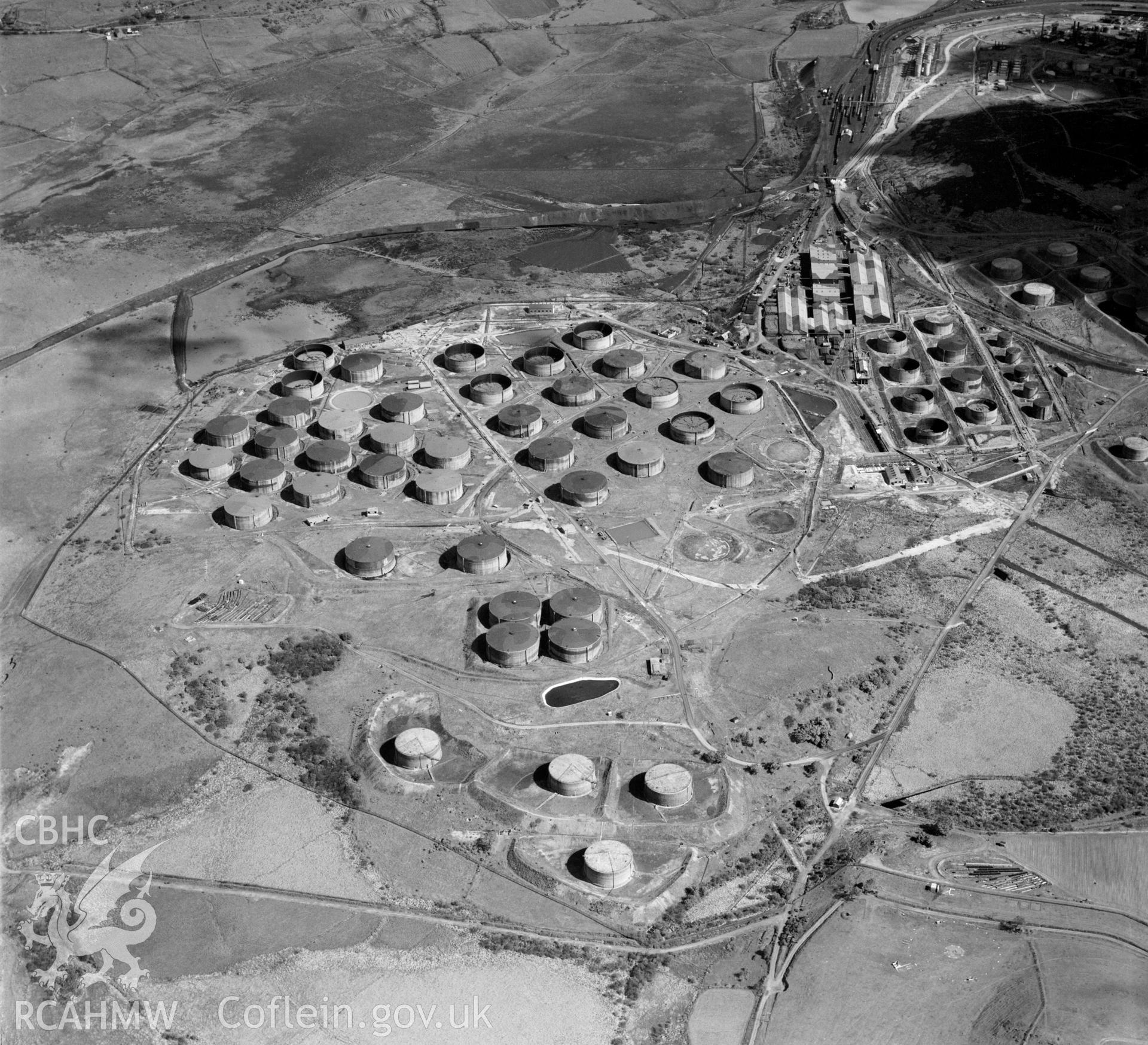 Digital copy of a black and white, oblique aerial photograph of Llandarcy oil refinery. The photograph shows a view from the South. This refinery was the first oil refinery in Wales and built in the 1920s. It was an important target for enemy bombers during World War 2, note the buildings in the top right of the photograph that still retain their wartime camouflage.