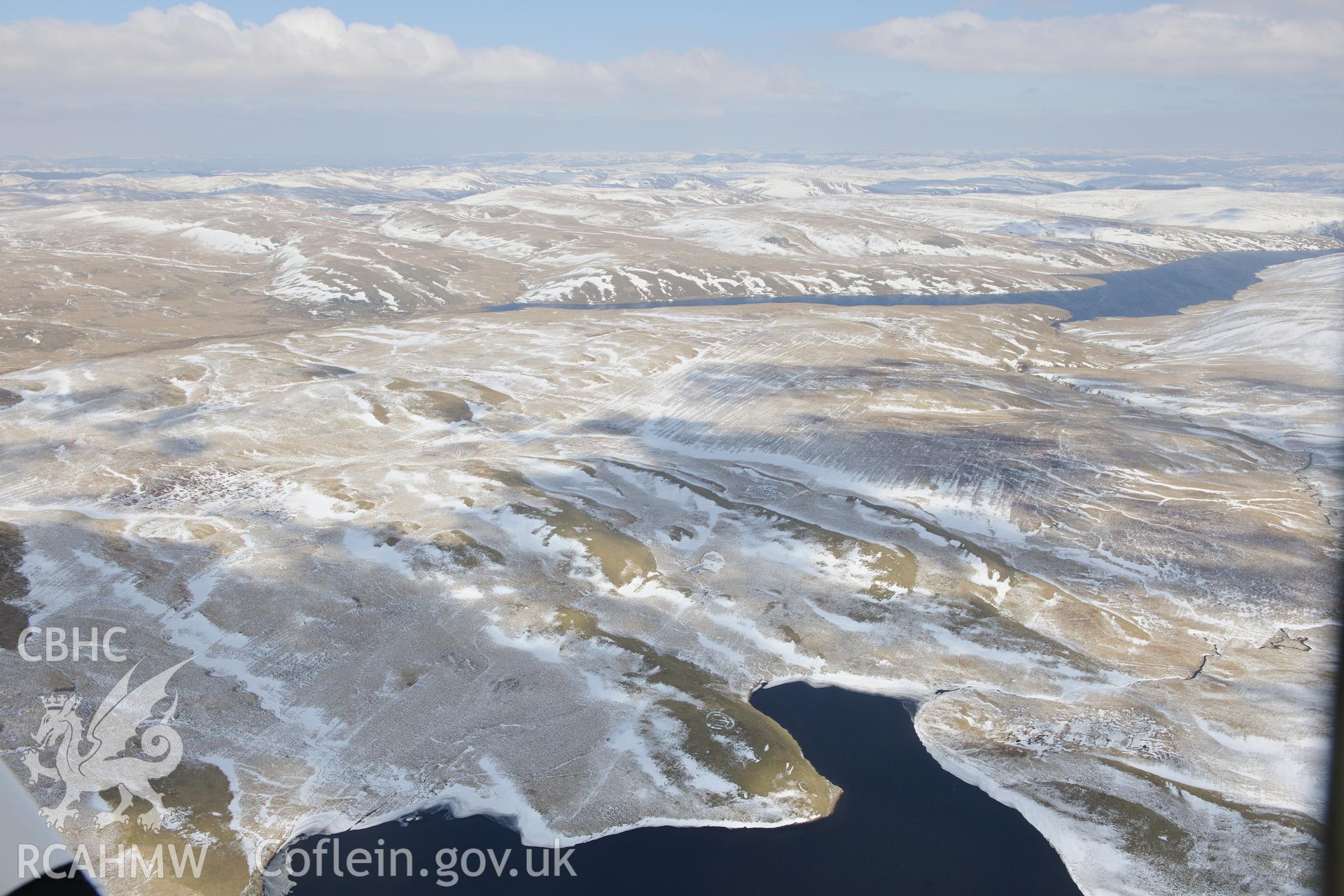 An enclosure and long house on the shores of Llyn Gynon, with a view of the Cambrian Mountains beyond. Oblique aerial photograph taken during the Royal Commission's programme of archaeological aerial reconnaissance by Toby Driver on 2nd April 2013.