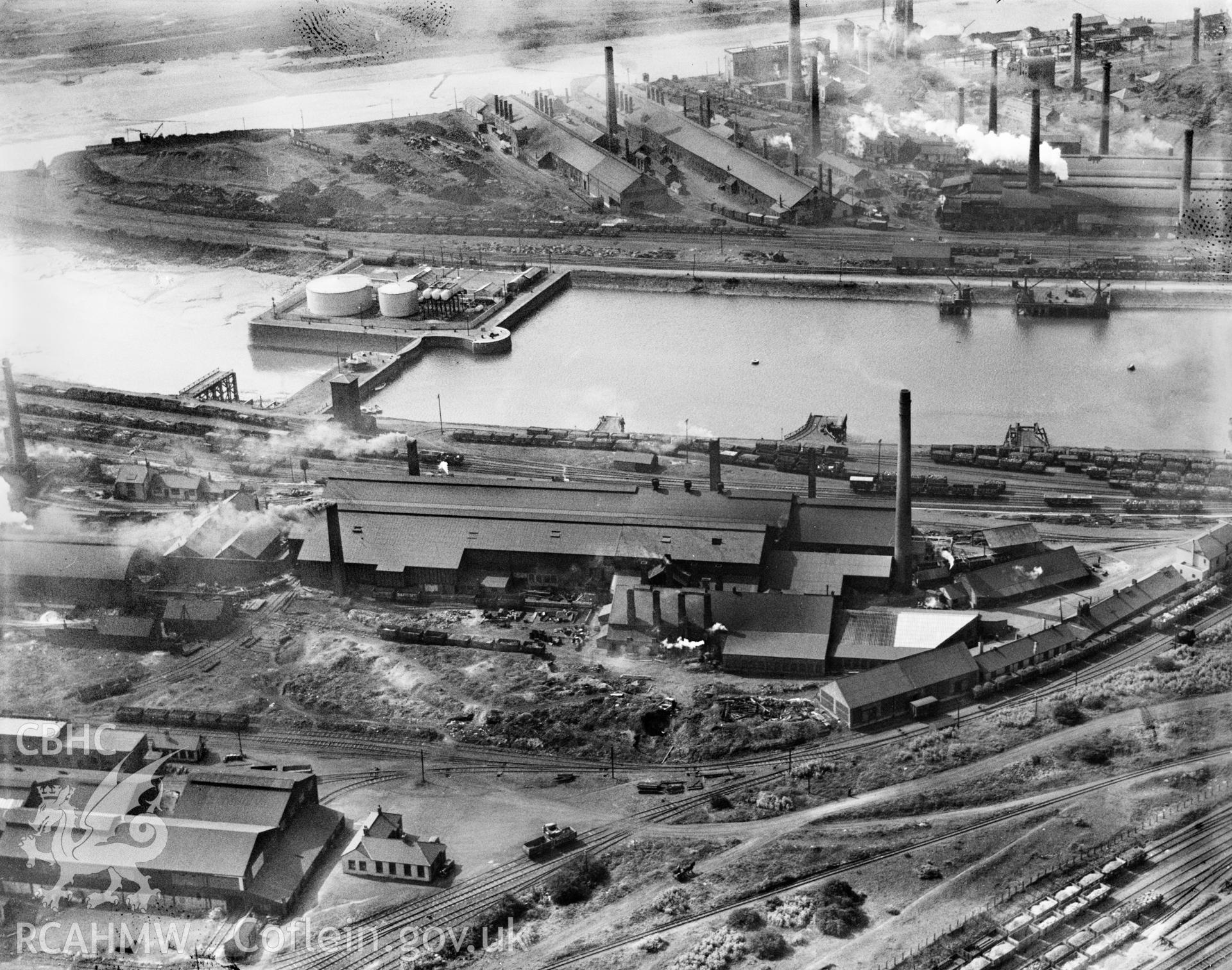 View of Baglan Bay Timplate Co., Briton Ferry showing dock and Albion works in foreground, with Cambrian cokeworks, Gwalia, Victoria and Briton Ferry steelworks, oblique aerial view. 5?x4? black and white glass plate negative.