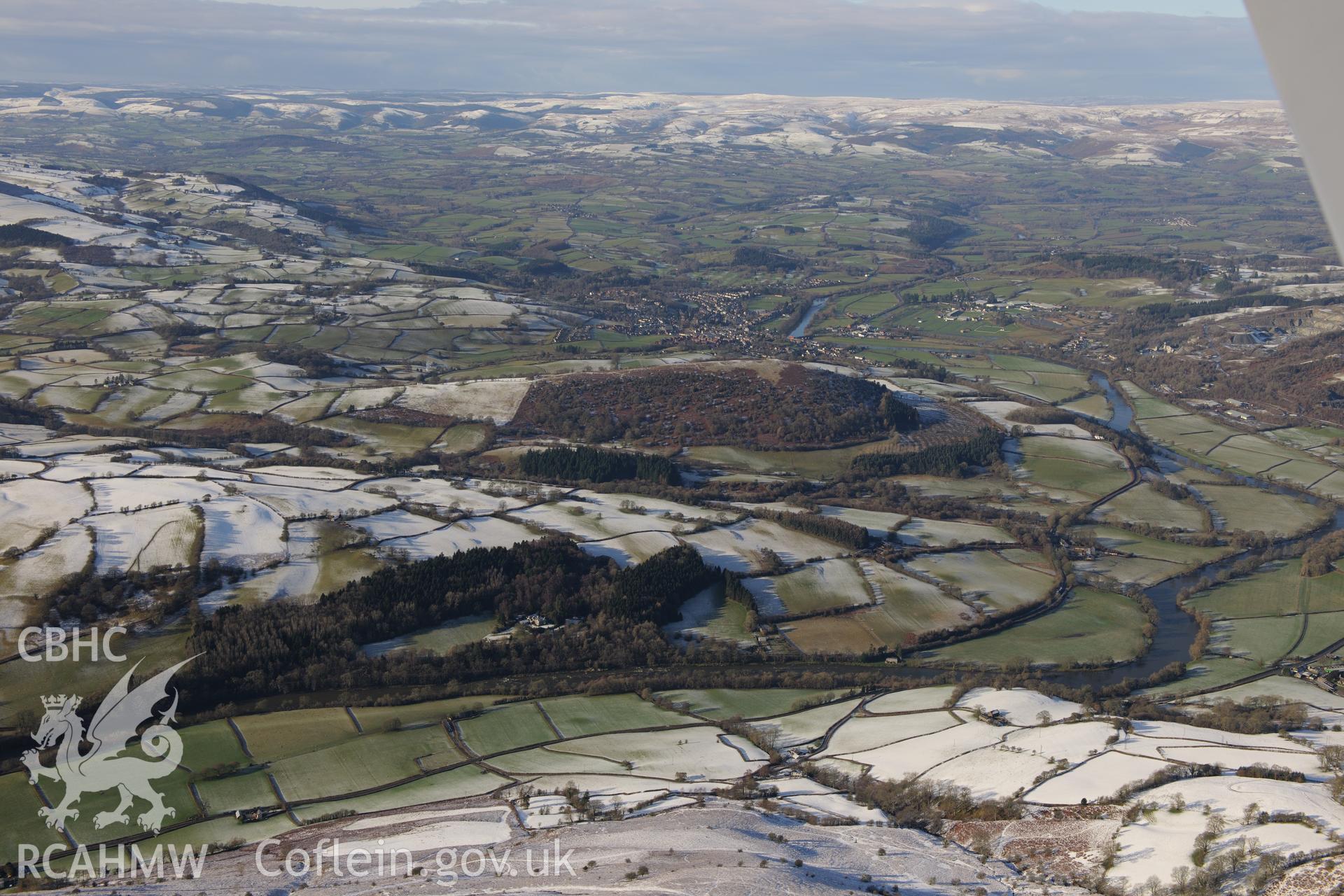 Garth hill, with the river Wye to the left of the photograph, and the town of Builth Wells and the Royal Welsh Showground in the distance beyond. Oblique aerial photograph taken during the Royal Commission?s programme of archaeological aerial reconnaissance by Toby Driver on 15th January 2013.