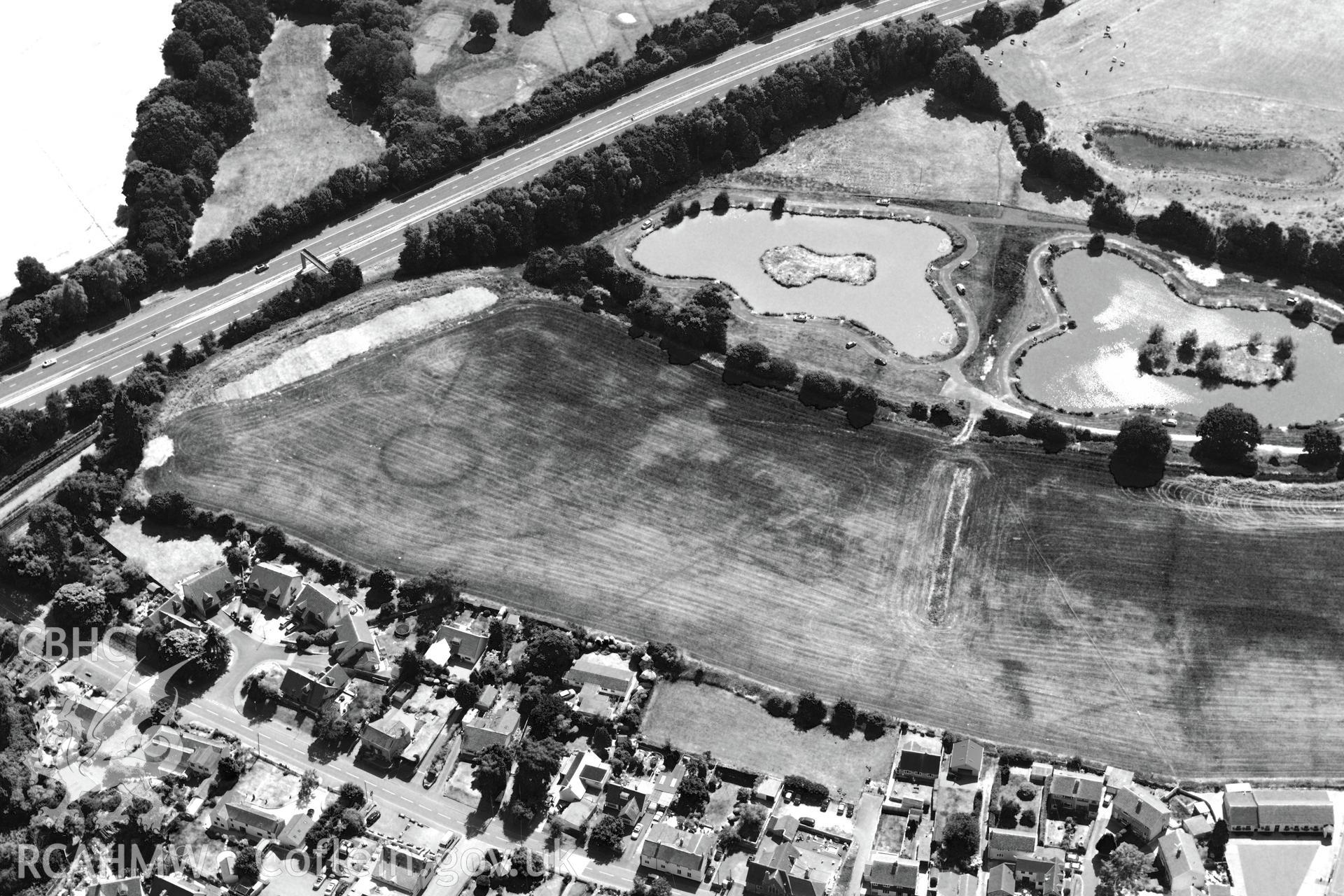 Round barrow cropmarks and the village of Newton Green,south west of Chepstow, with the M48 passing to the south. Oblique aerial photograph taken during the Royal Commission?s programme of archaeological aerial reconnaissance by Toby Driver on 1st August