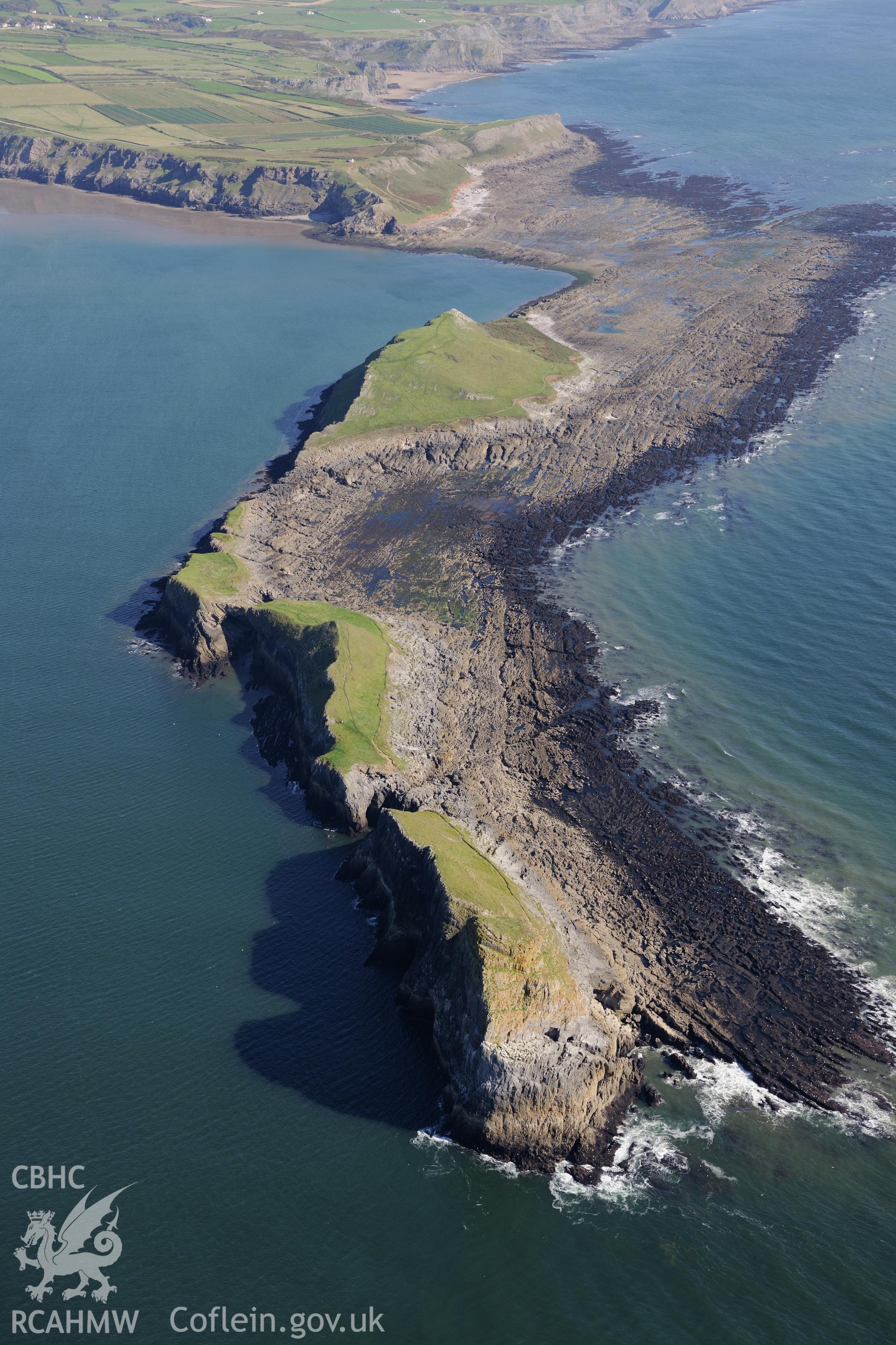 Worms Head, with Worms Head Cave in the foreground and Worm sound at low tide beyond. Oblique aerial photograph taken during the Royal Commission's programme of archaeological aerial reconnaissance by Toby Driver on 30th September 2015.