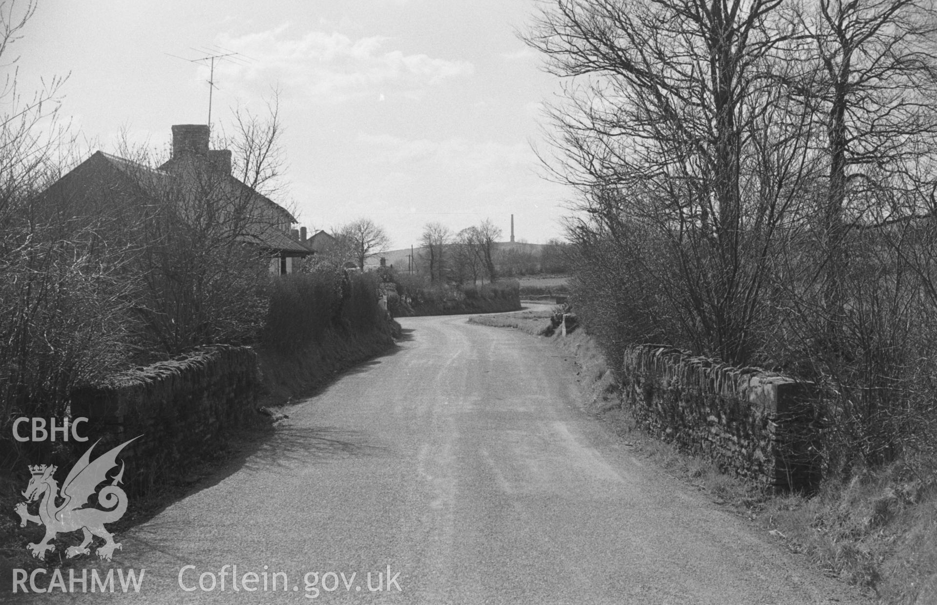 Digital copy of a black and white negative looking along the Lampeter Road from bridge over the Afon Dulas. Derry-Ormond tower on centre skyline. Photographed by Arthur O. Chater in April 1966 from Grid Reference SN 605 528, looking south west.