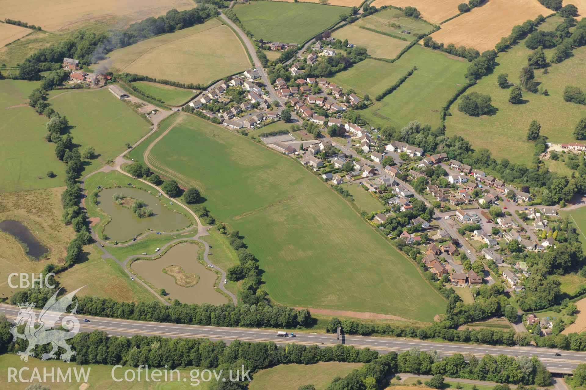 Round barrow cropmarks and the village of Newton Green,south west of Chepstow, with the M48 passing to the south. Oblique aerial photograph taken during the Royal Commission?s programme of archaeological aerial reconnaissance by Toby Driver on 1st August