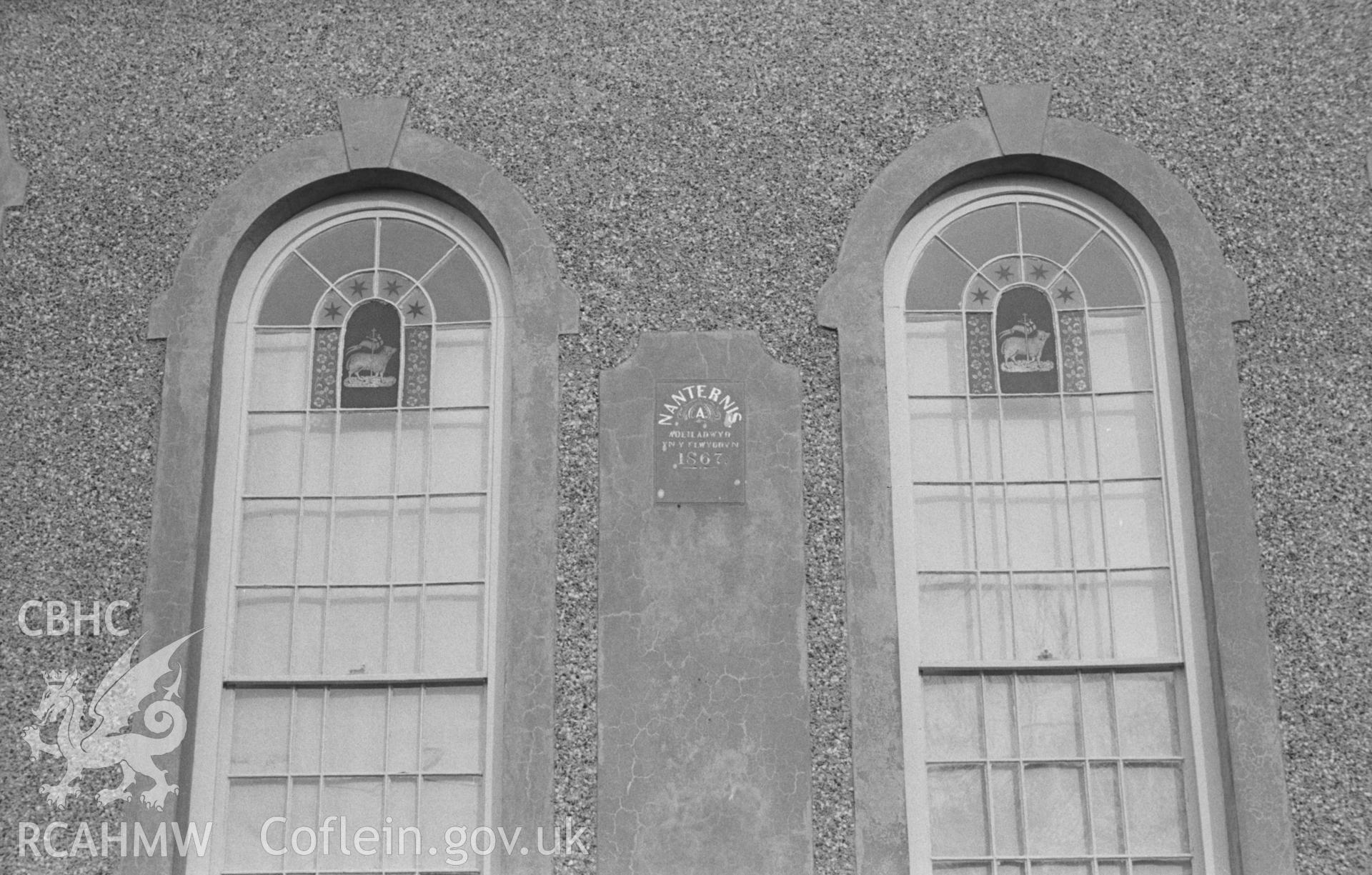 Black and White photograph showing Nanternis Chapel exterior. Two windows with stained glass 'Agnus Dei' on the north western front of the chapel (1867). Photographed by Arthur Chater in April 1963 from Grid Reference SN 372 565, looking south east.