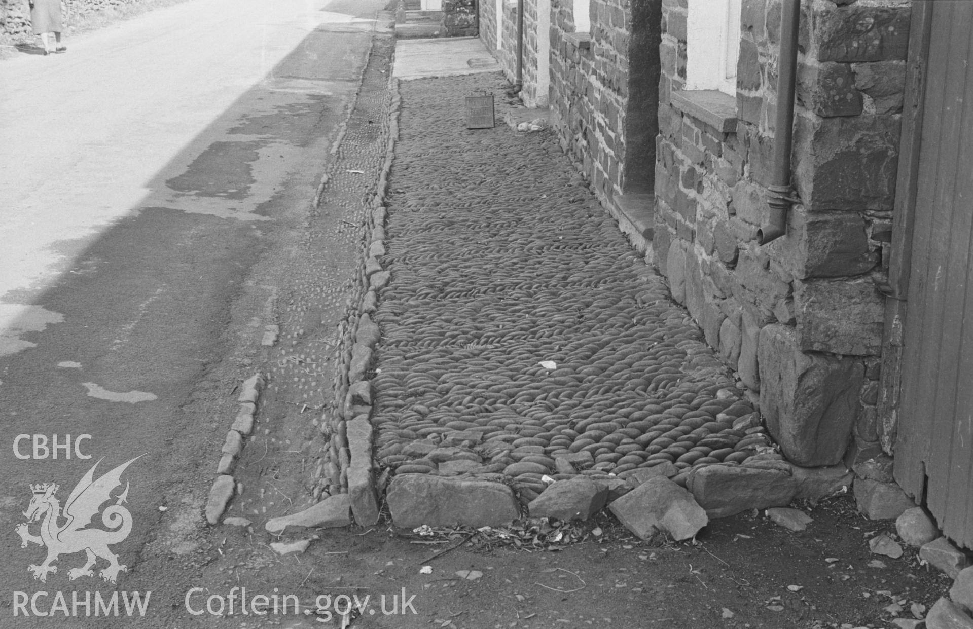 Black and White photograph showing cobbled pavement and gutter on the south east side of Moelivor Terrace at Llanrhystyd. Photographed by Arthur Chater in April 1963 from Grid Reference SN 540 697, looking north east.