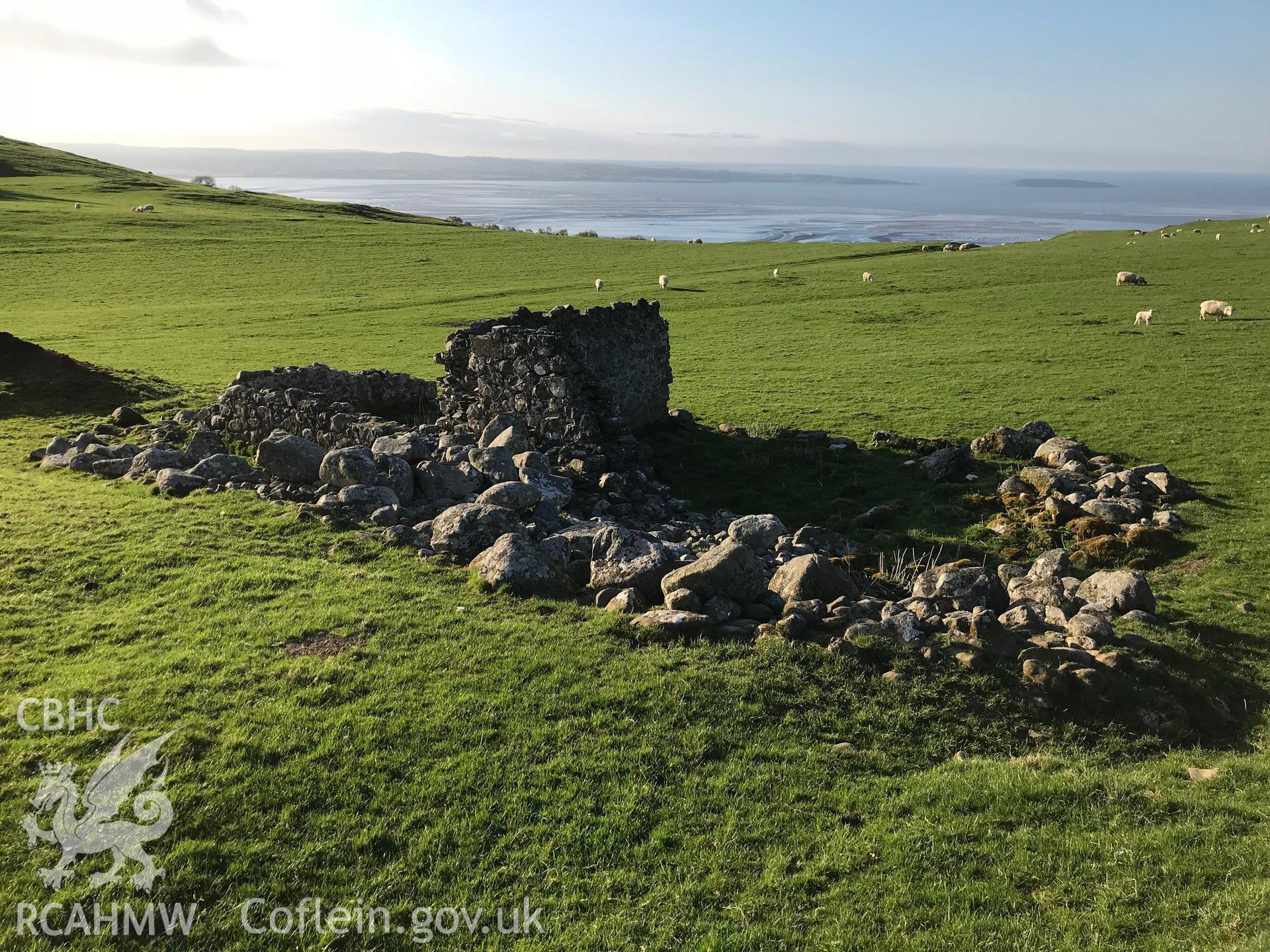 Colour photo of ruined 2 roomed building 600m west of Bod Silin house, presumably a field barn. The stonework suggests no great age. Since used as a dump for larger boulders gathered from surrounding fields (SH 666 727), taken by Paul R. Davis 19/4/2018.