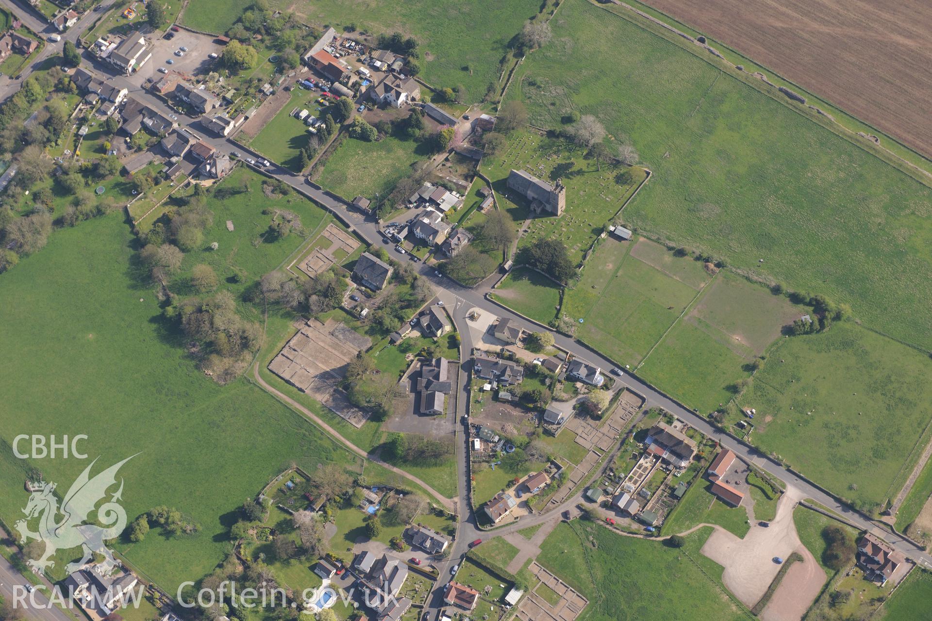 Caerwent village and Roman city including views of the Roman Amphitheatre and Basilica and Forum; St. Stephen's Church; Caerwent House; Great House and West Gate Farm. Oblique aerial photograph taken during the Royal Commission's programme of archaeological aerial reconnaissance by Toby Driver on 21st April 2015.