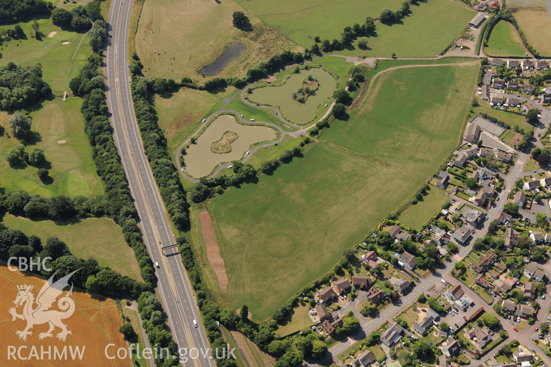 Round barrow cropmarks and the village of Newton Green,south west of Chepstow, with the M48 passing to the south. Oblique aerial photograph taken during the Royal Commission?s programme of archaeological aerial reconnaissance by Toby Driver on 1st August