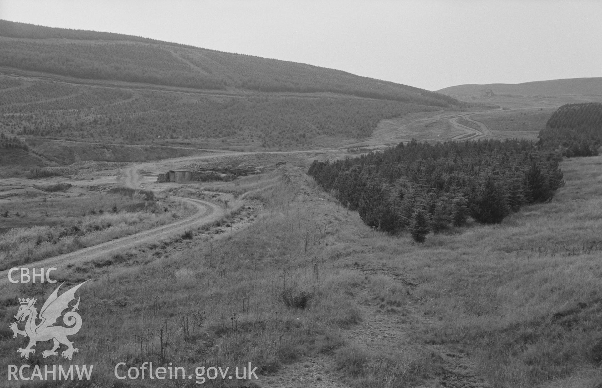 Digital copy of a black and white negative showing view looking along raised bank of (?)tramway to the wheel pit of Esgair Fraith lead mine. Photographed by Arthur O. Chater on 22nd August 1967, looking west south west from Grid Reference SN 742 912.