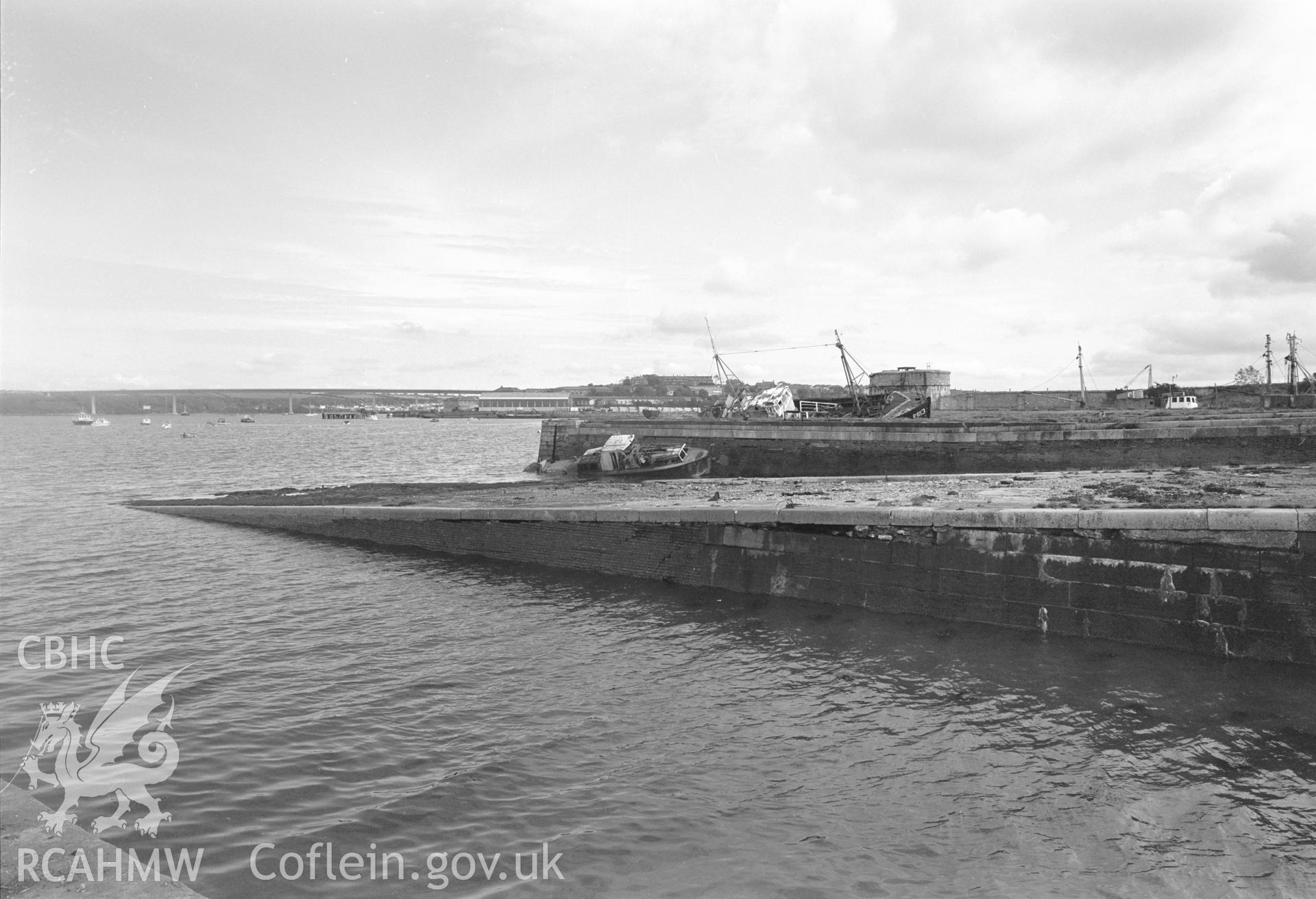 Digital copy of a black and white negative showing Old Royal Dockyard Pembroke. Looking E over ship building slip 11 to smaller seaplane launching ramp with building slip 12 and pier beyond, E Martello Tower in distance., taken by RCAHMW.