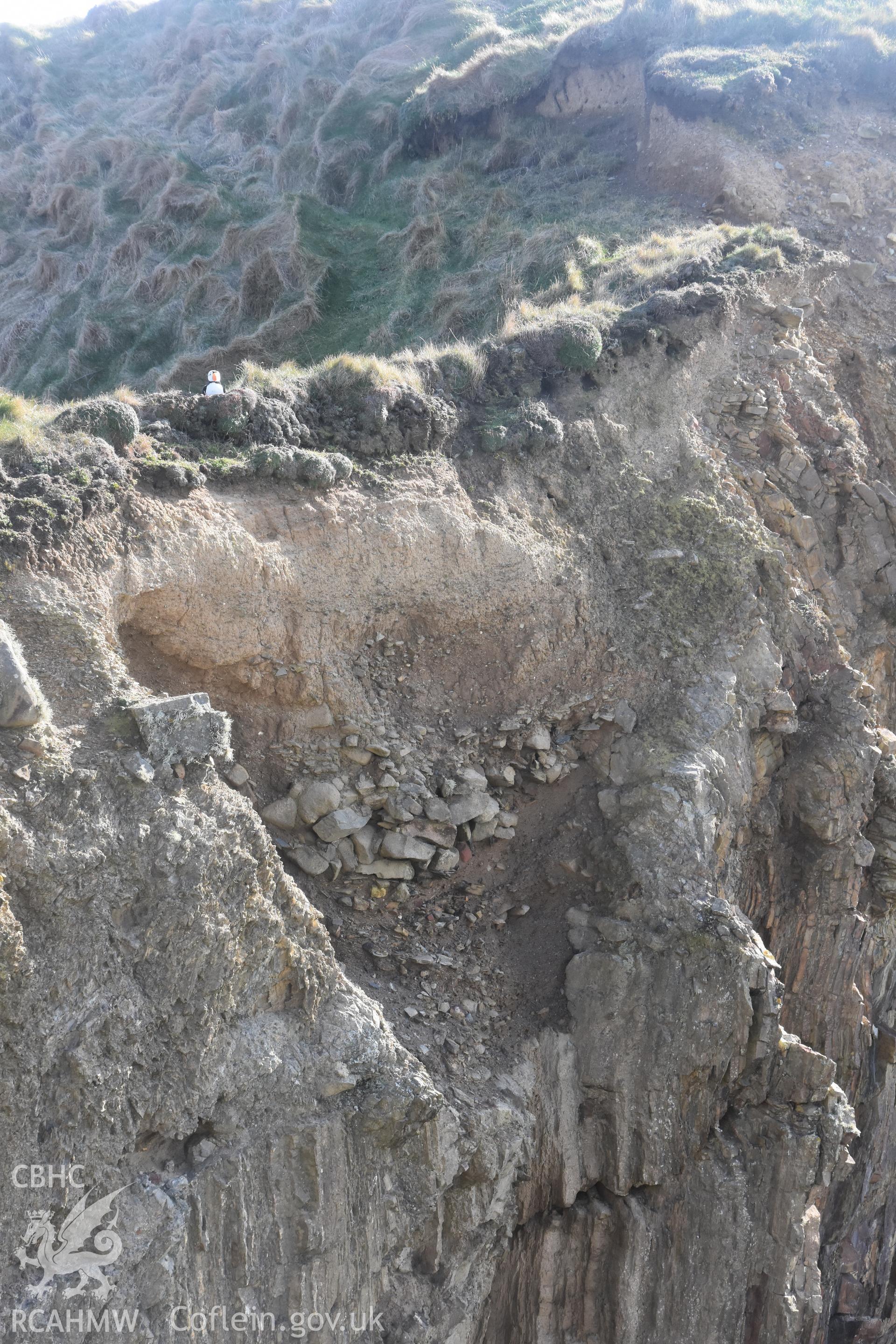 Porth y Rhaw promontory fort. Photograph of eroded section through western rock-cut ditch. ? Crown: CHERISH PROJECT 2017. Produced with EU funds through the Ireland Wales Co-operation Programme 2014-2020. All material made freely available through the Open Government Licence.