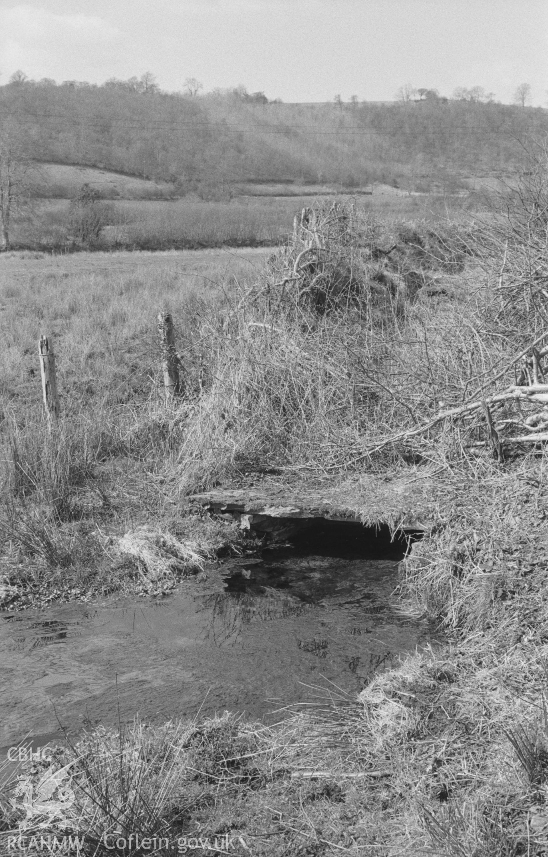 Digital copy of black & white negative showing Ffynnon Gybi, now covered by large slate slab. Very clear water beneath, reached by short path from road opposite chapel at south west end of Llangybi. Photograph by Arthur O. Chater, April 1966, SN 605 528.